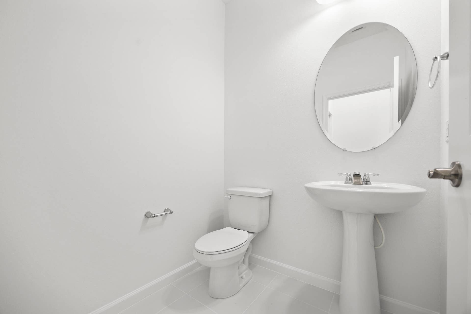 Pedestal sink with chrome-finish faucet, oval mirror, wall-mounted light fixture, and toilet