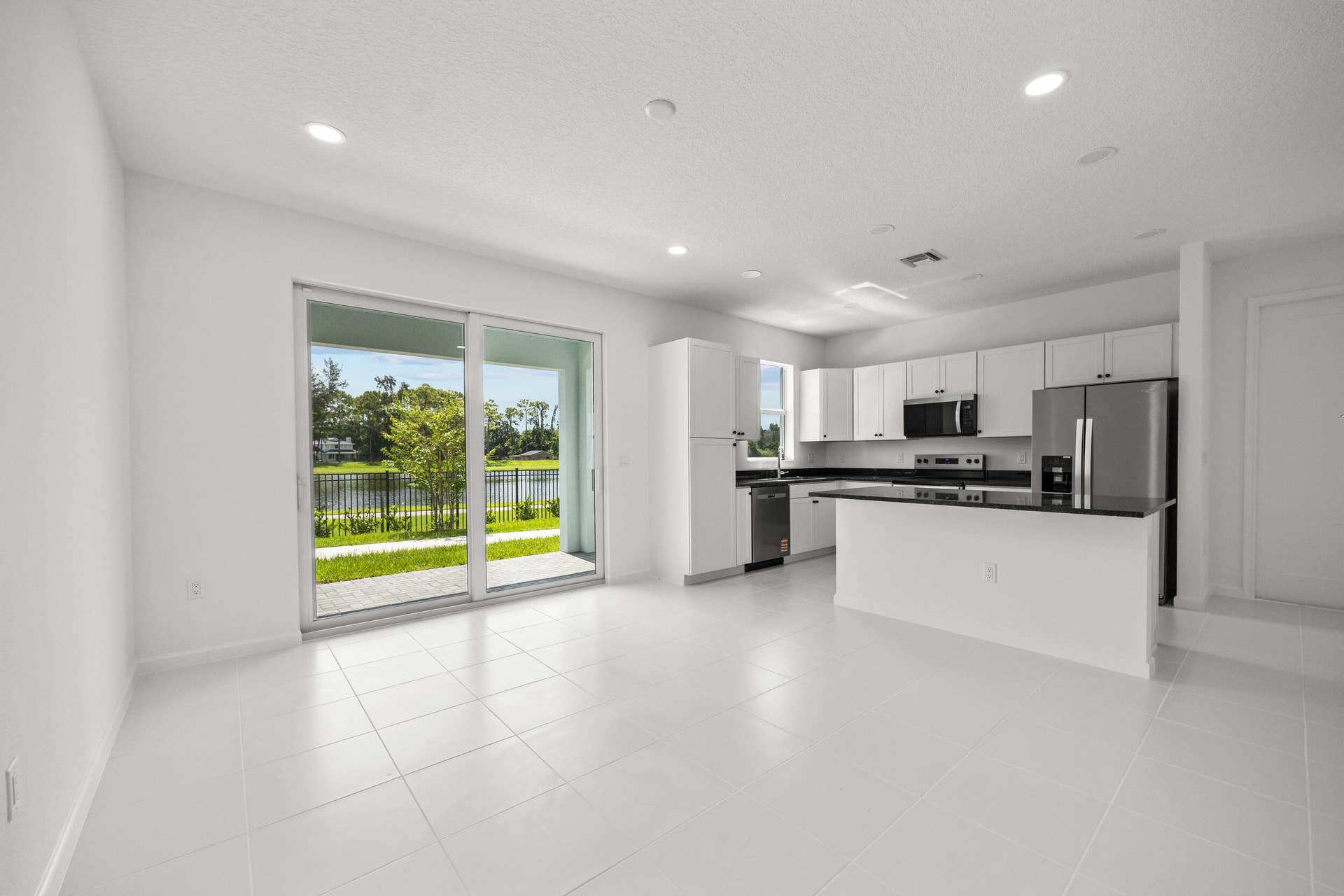 Spacious interior with white tile flooring, white cabinetry, stainless steel appliances, and a kitchen island with a dark countertop