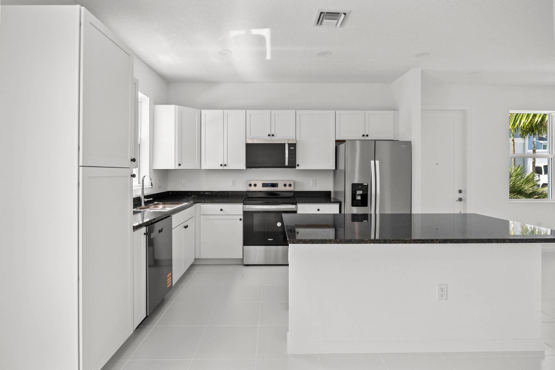 White shaker cabinetry, dark countertops, tile flooring, stainless steel appliances, and a kitchen island