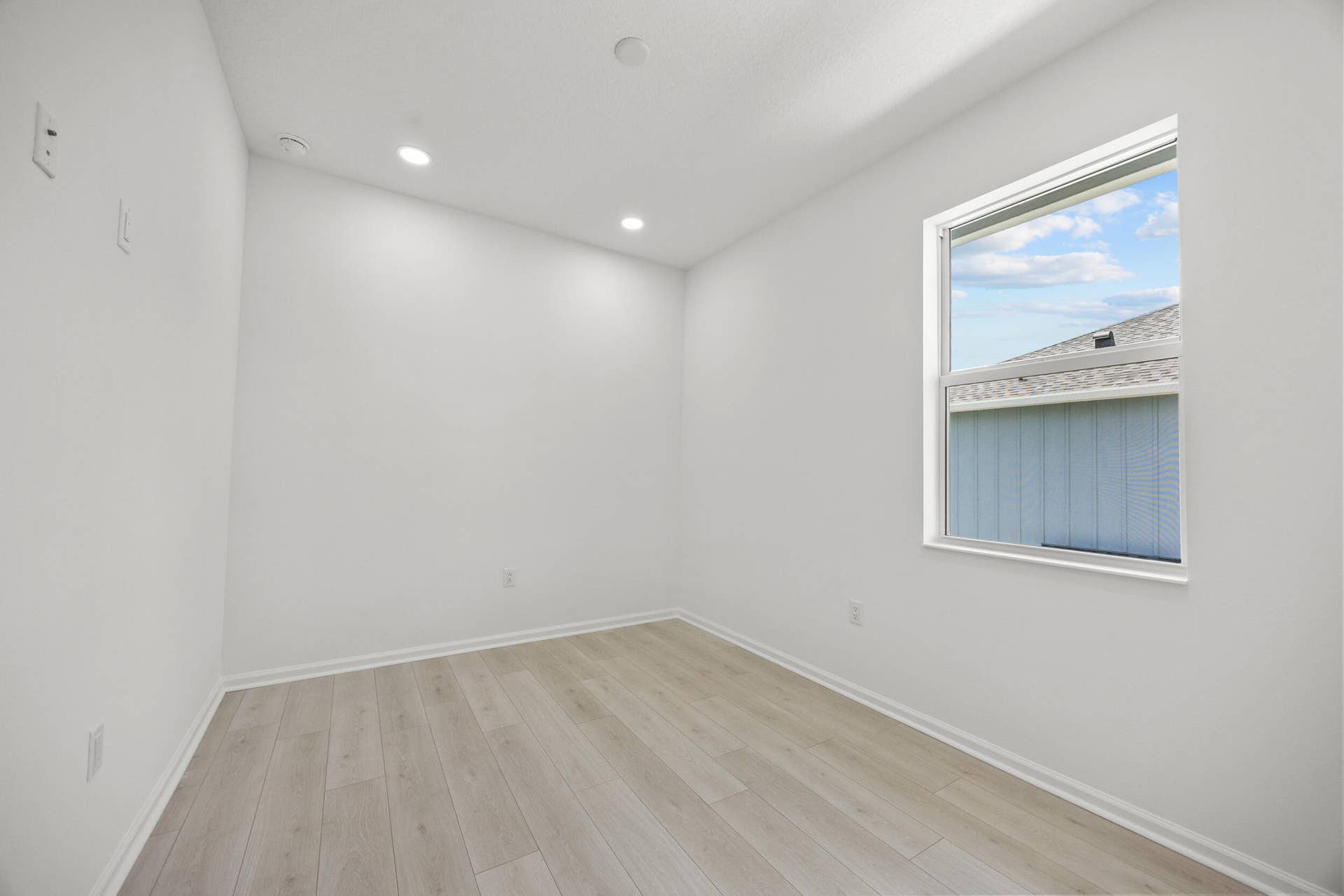 Recessed ceiling lighting, wood-finish flooring, white wall paint, and a single window with white trim