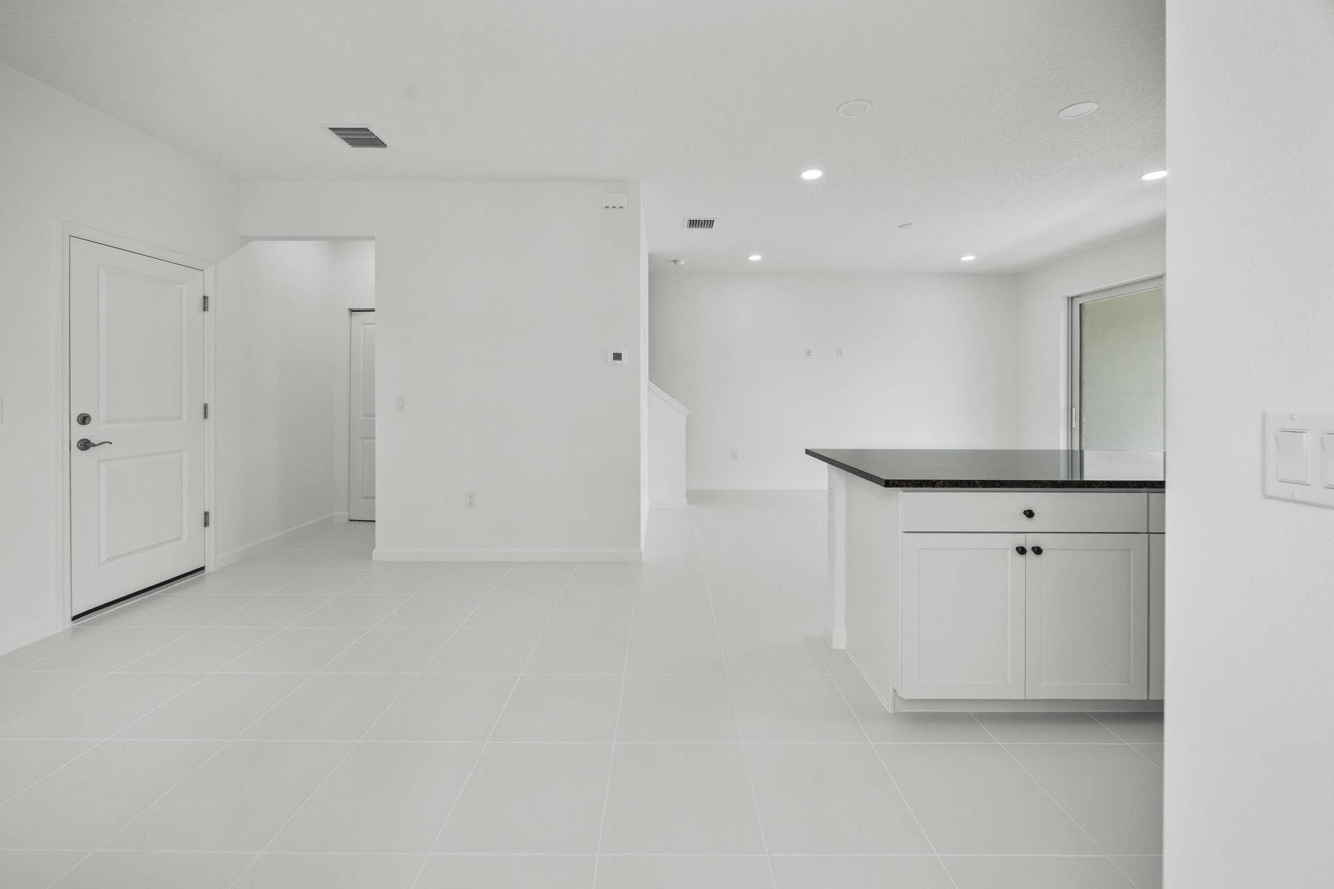 Kitchen island with white cabinetry and dark countertop, recessed lighting, white tile flooring, and sliding glass door