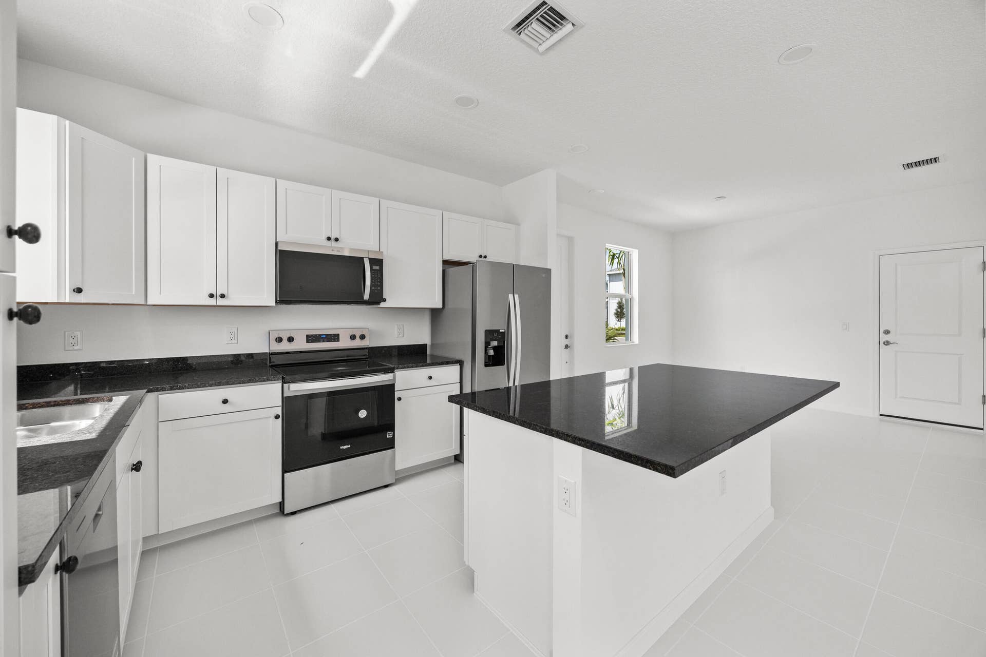 Kitchen featuring dark countertops, white cabinetry, stainless steel appliances, a kitchen island, and tile flooring