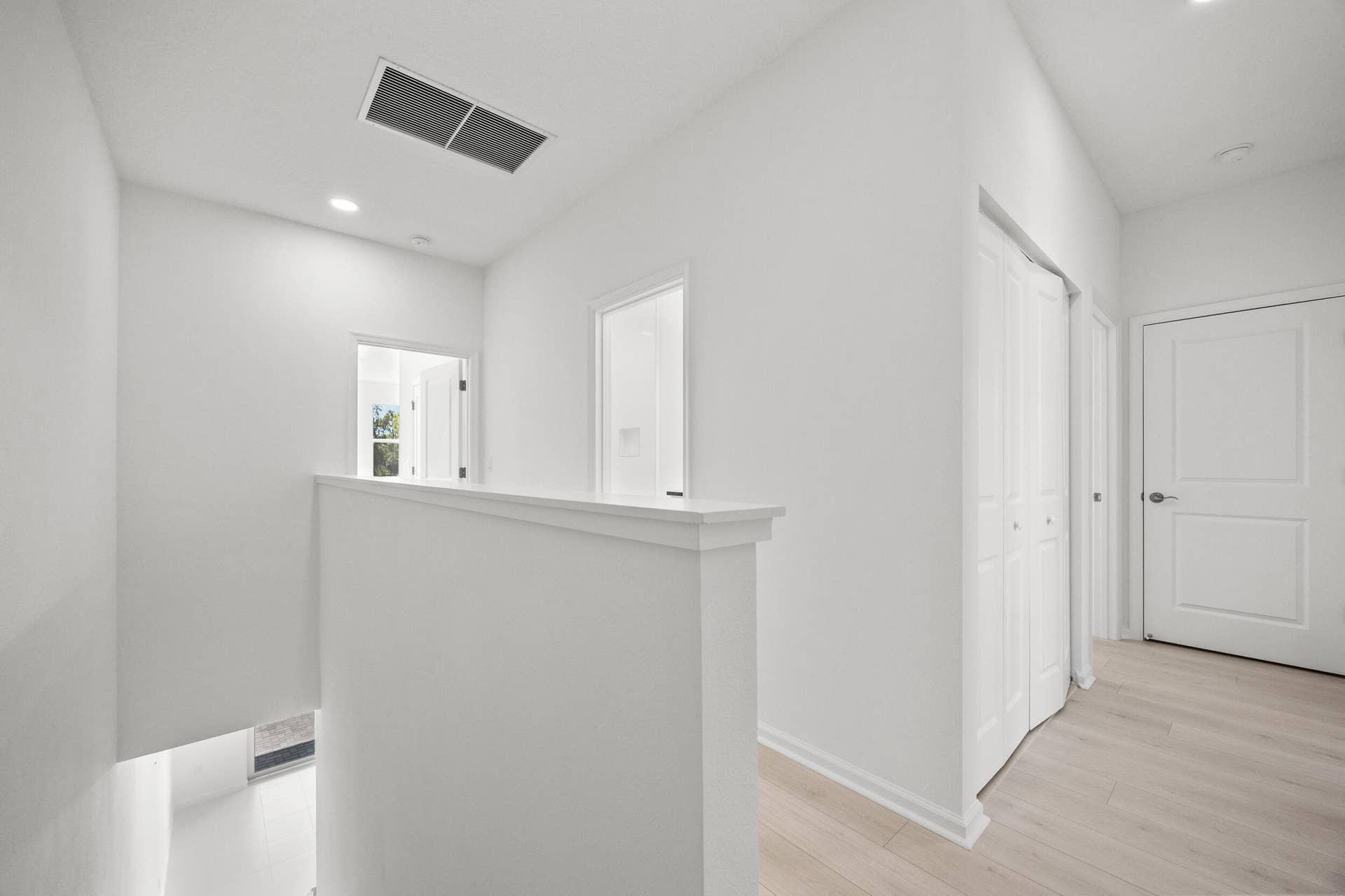 Light wood-finish flooring, white walls, recessed ceiling lighting, and white bi-fold closet doors