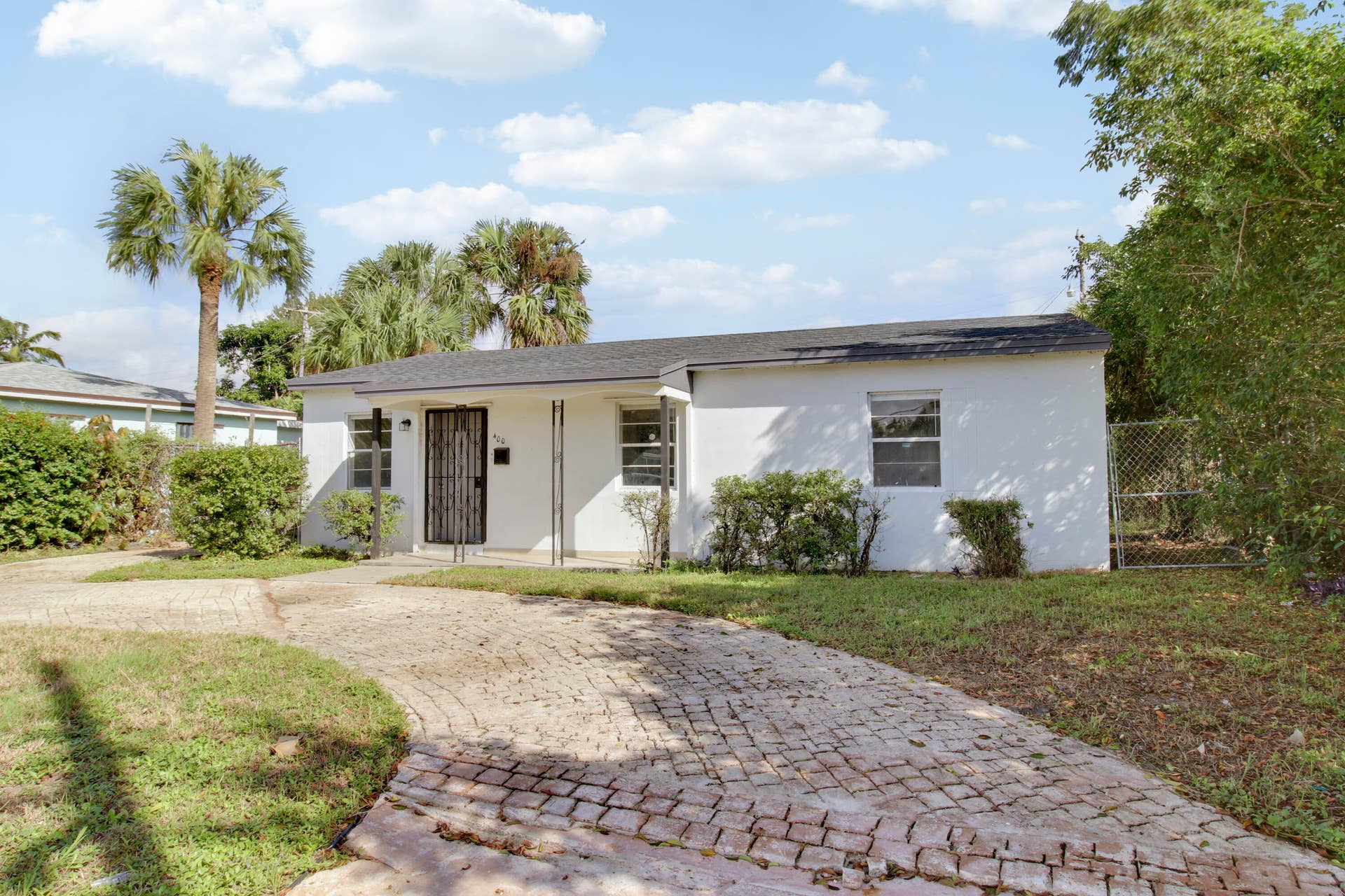 Single-story exterior with white stucco finish, dark shingle roof, and a paver driveway