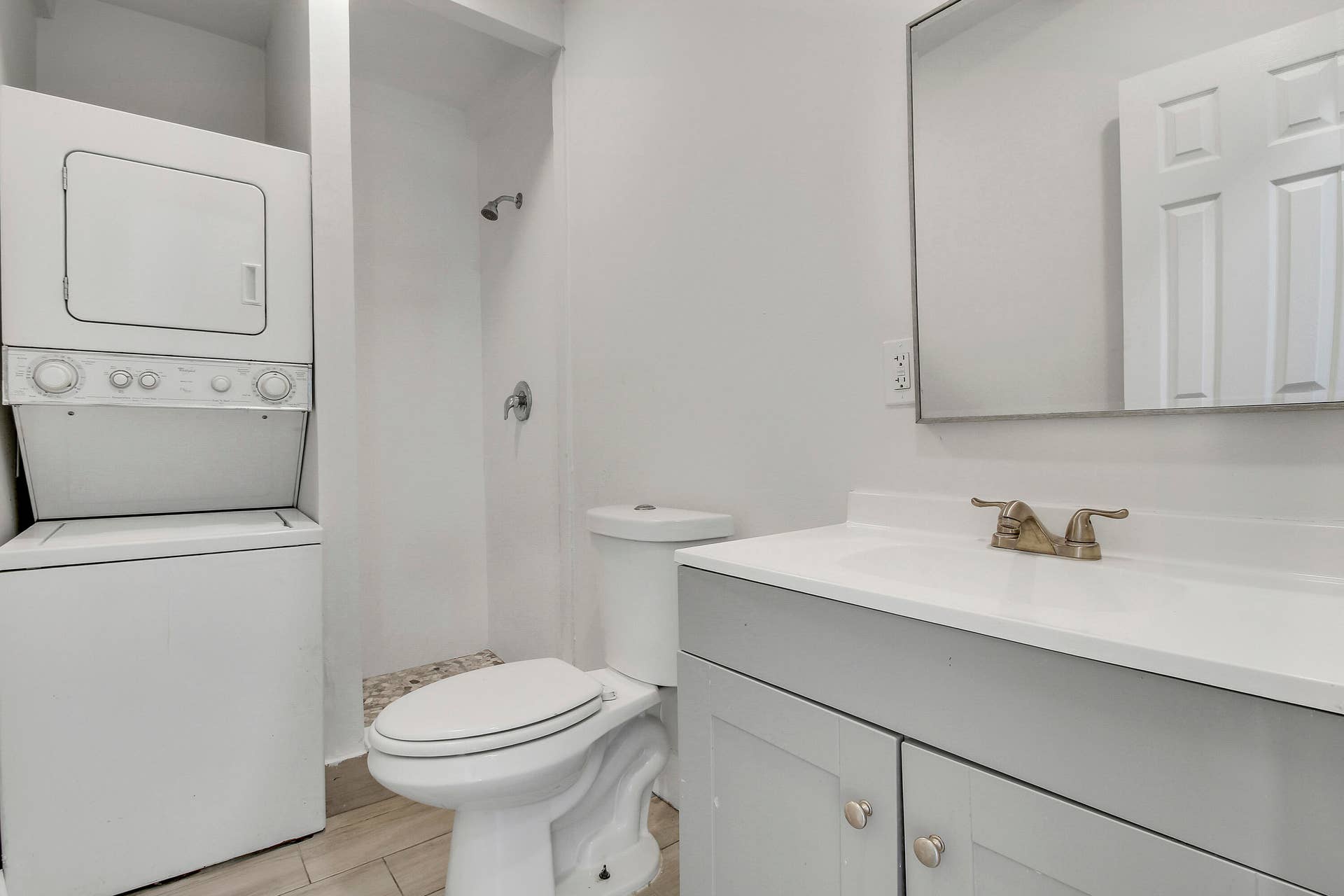 White stackable washer and dryer, light gray vanity with white countertop, chrome faucet, and rectangular mirror