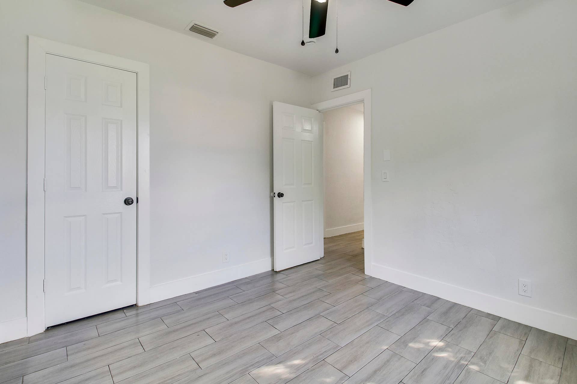 Neutral tone walls with light-colored tile flooring, white six-panel doors, and a ceiling fan with integrated lighting