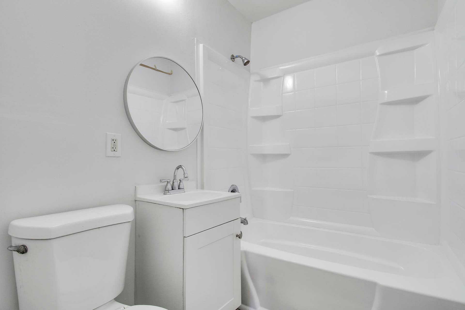 White vanity with chrome faucet, circular mirror, and combination shower/tub with integrated shelving