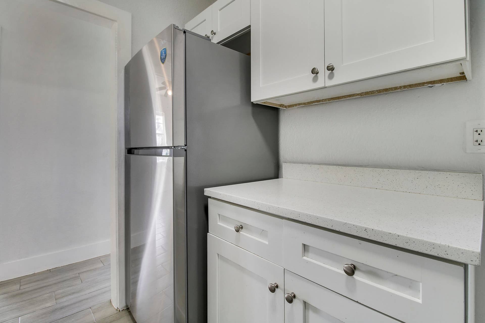 Stainless steel refrigerator, white shaker-style cabinetry, and light-toned countertops