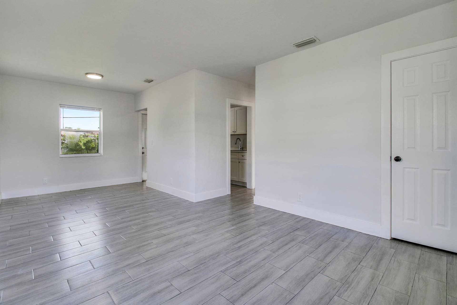 Spacious room with light gray plank-style tile flooring, white walls, and a window