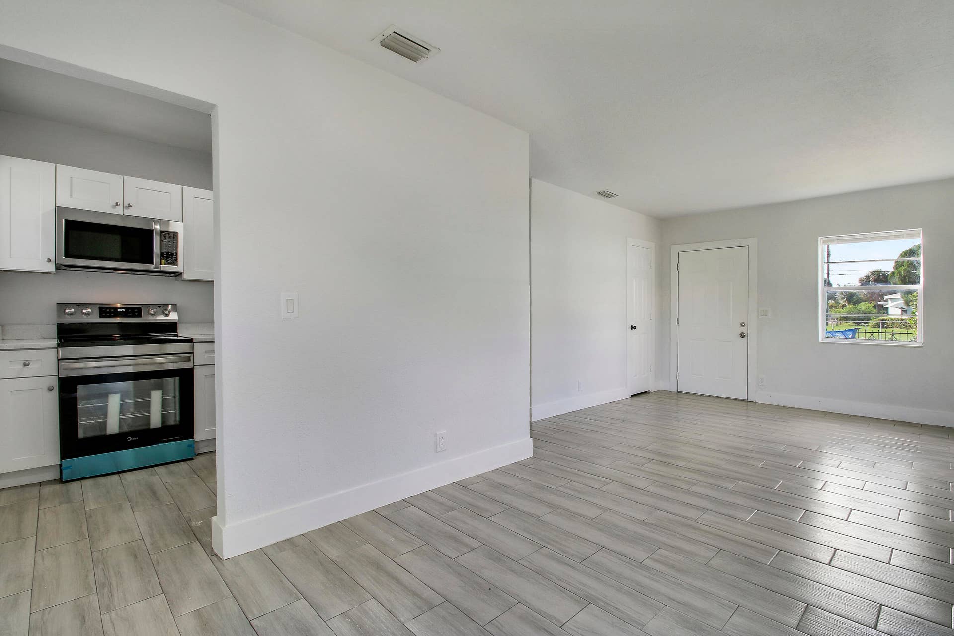 Open-concept living space with wood-finish tile flooring, white walls, and a large window