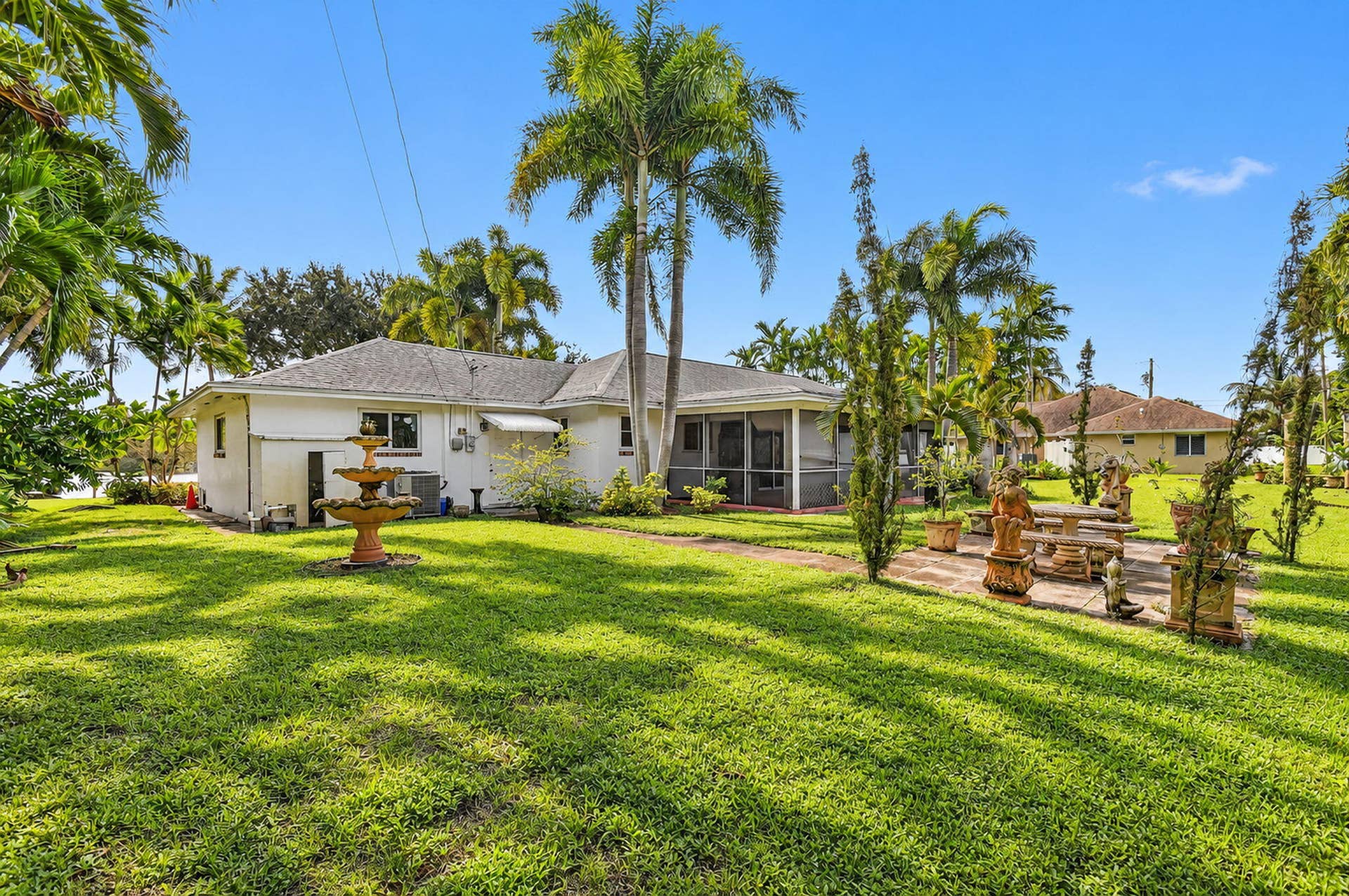 Expansive lawn with mature palm trees, a tiered fountain, and a screened-in patio
