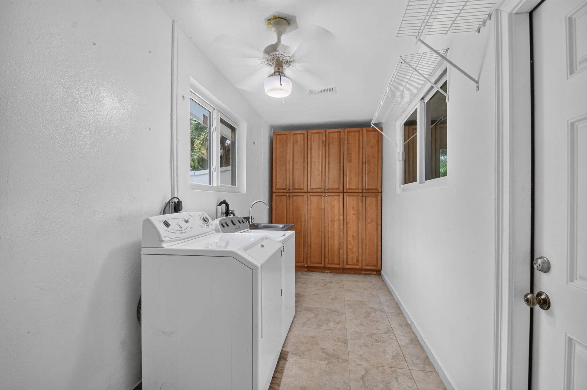 Utility room featuring tile flooring, built-in cabinetry, a ceiling fan, and a sink