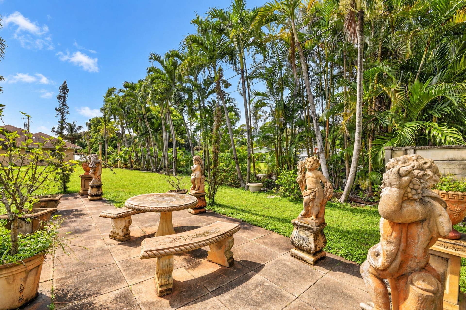 Patio with stone pavers, mature palm trees, grassy area, and decorative statues