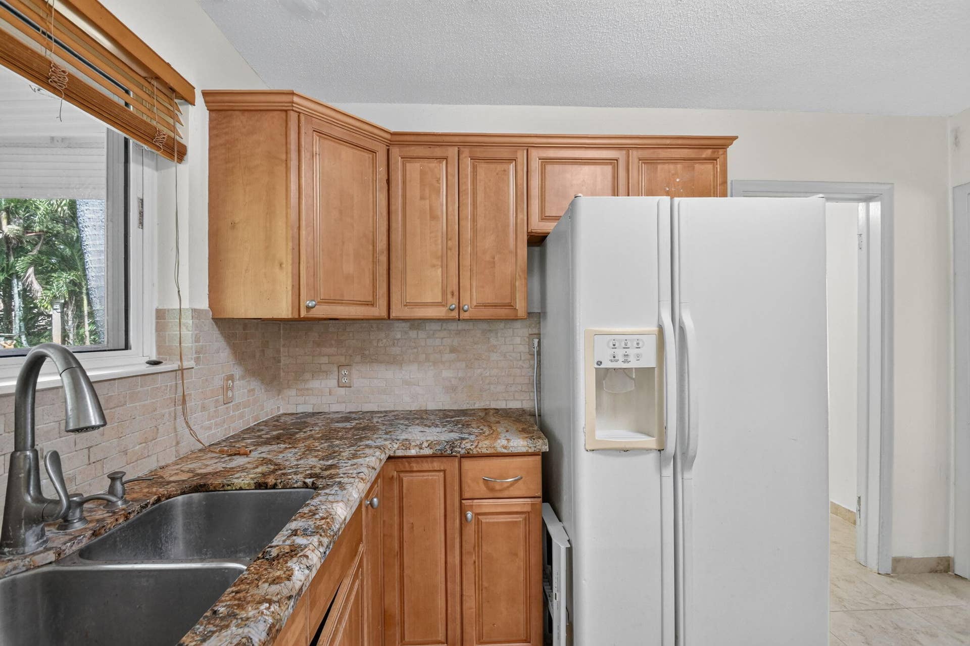 Kitchen featuring wood cabinetry, a stainless steel sink with a gooseneck faucet, patterned countertops, and a tiled backsplash