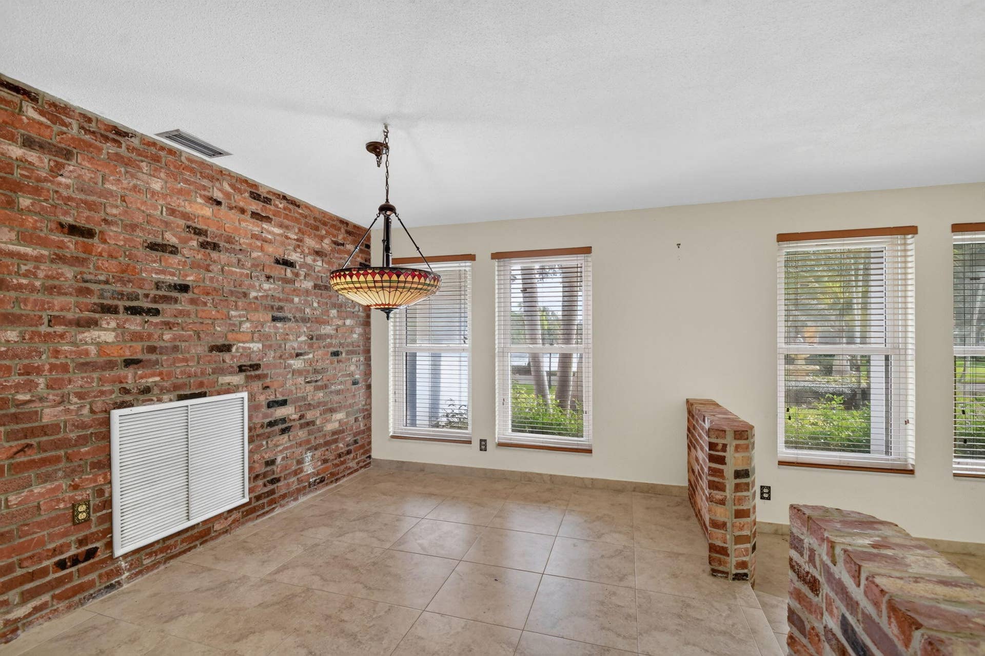 Exposed brick accent wall, tile flooring, multiple windows with blinds, brick half-wall, and a ceiling-mounted fixture