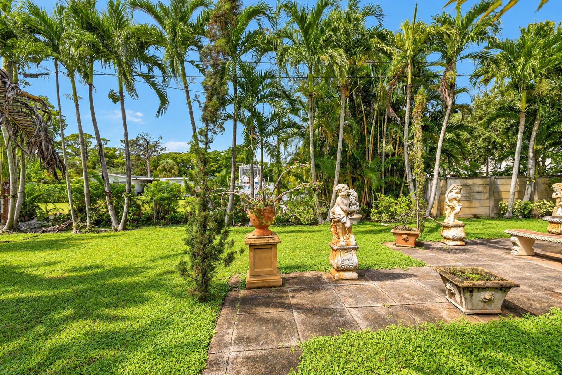 Manicured lawn with mature palm trees, flagstone patio, carved stone statuary, and built-in stone planter