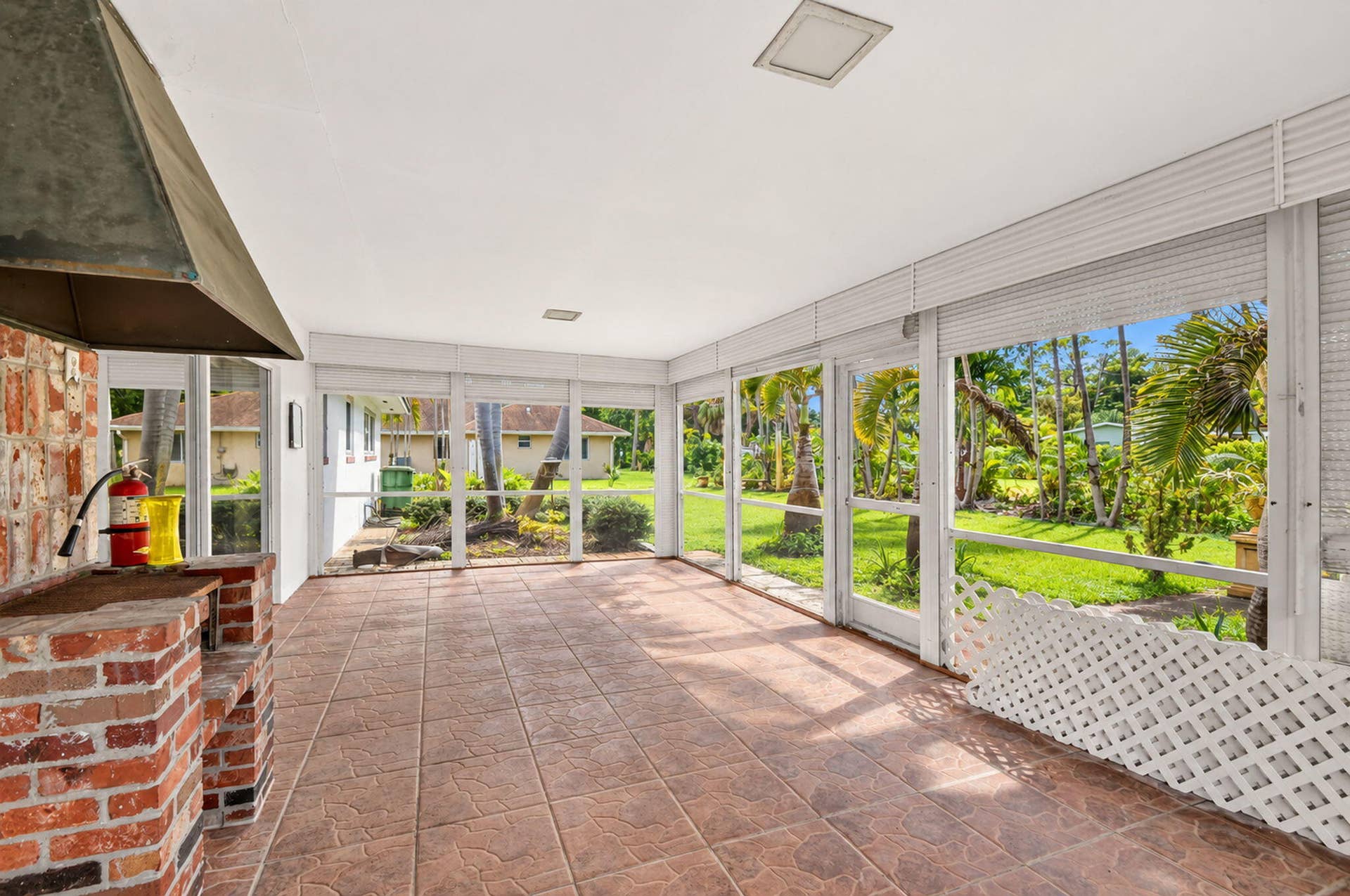 Expansive screened enclosure with a built-in brick grilling station, tile flooring, and a white ceiling