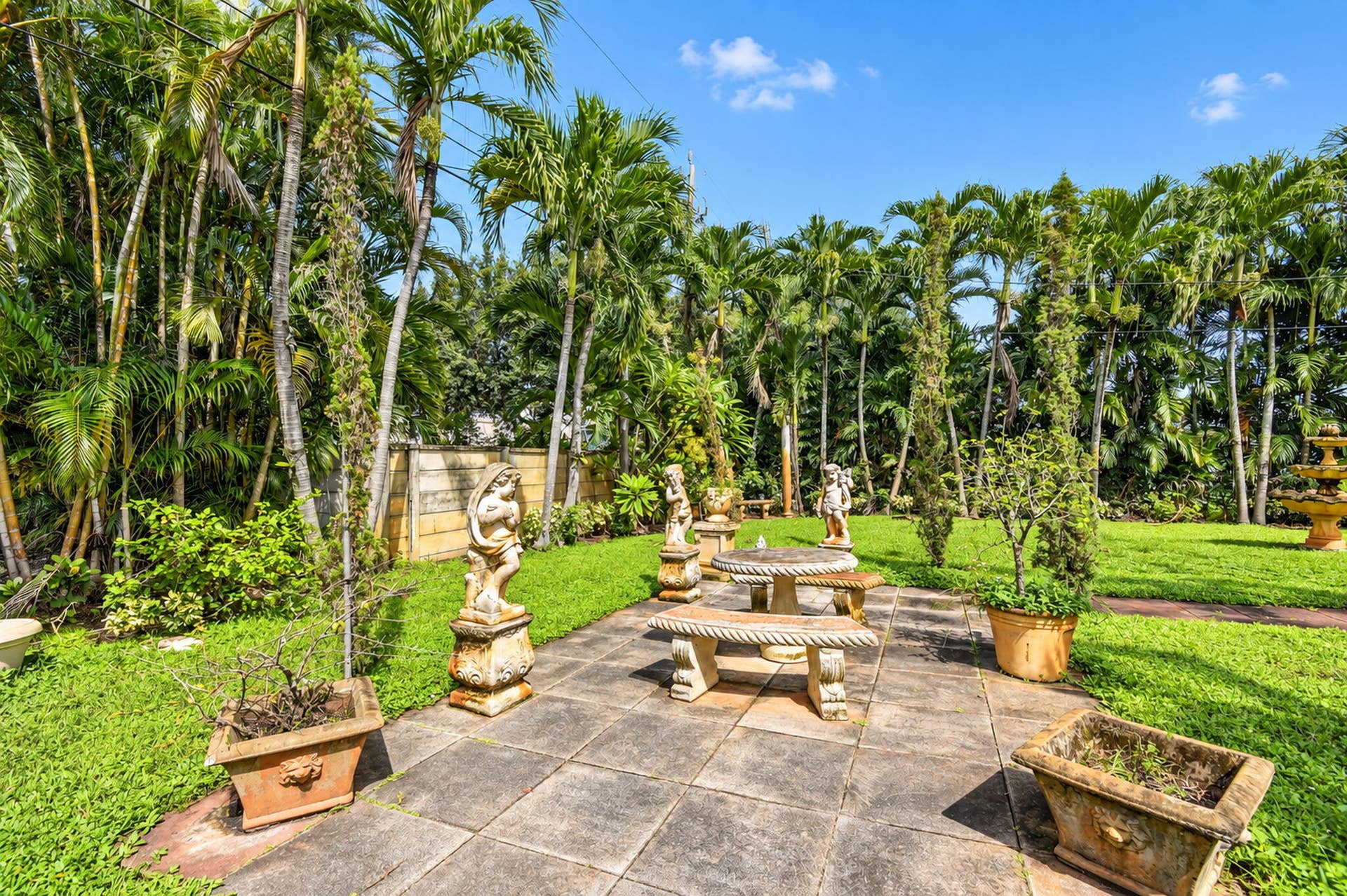 Expansive outdoor space featuring a stone-paver patio, a manicured lawn, and mature palm trees