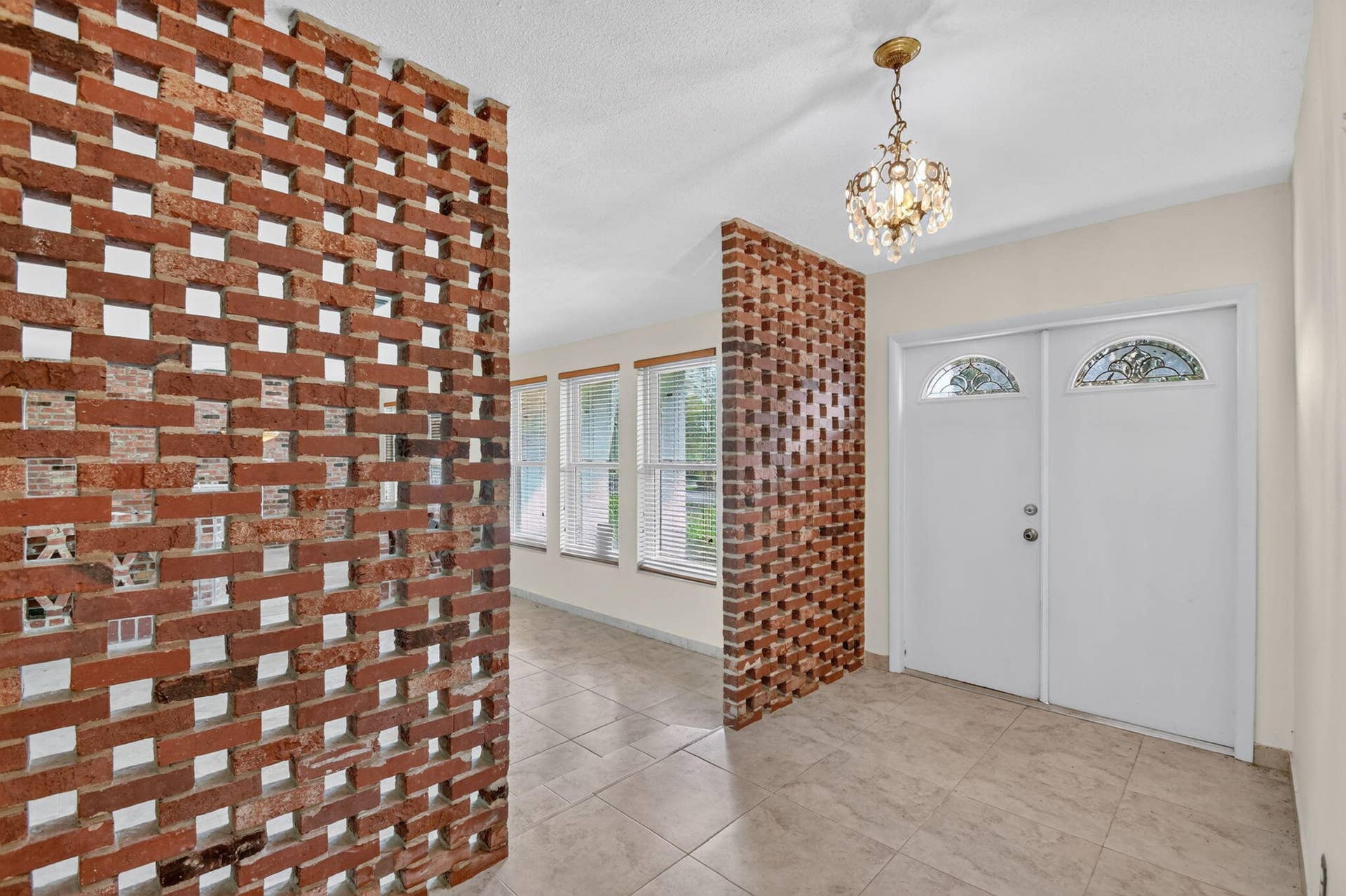 Brick screen wall, double entry doors with decorative glass transoms, tile flooring, and multiple windows