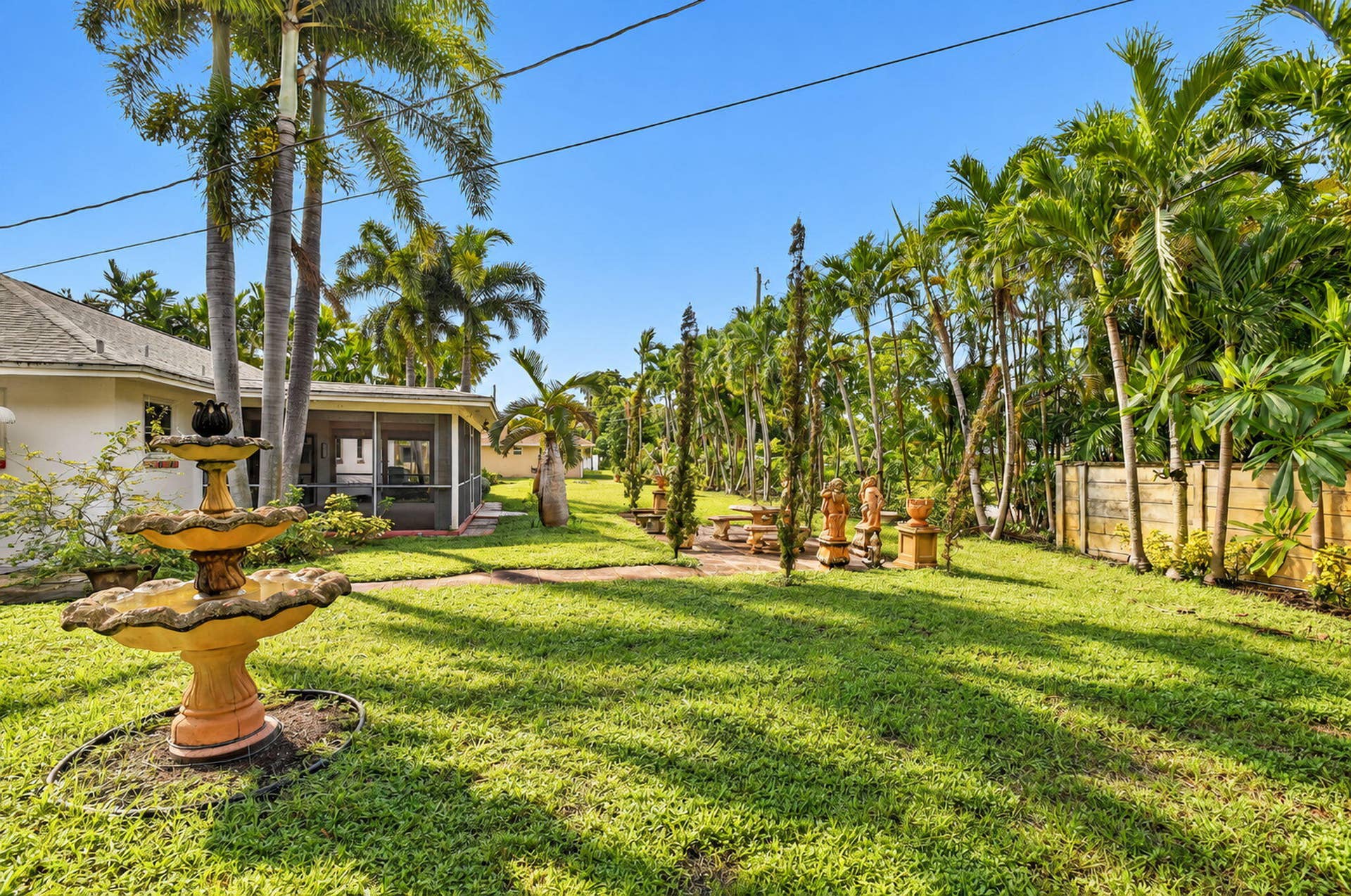 Expansive green lawn with mature palm trees, featuring a tiered outdoor fountain and a screened-in porch