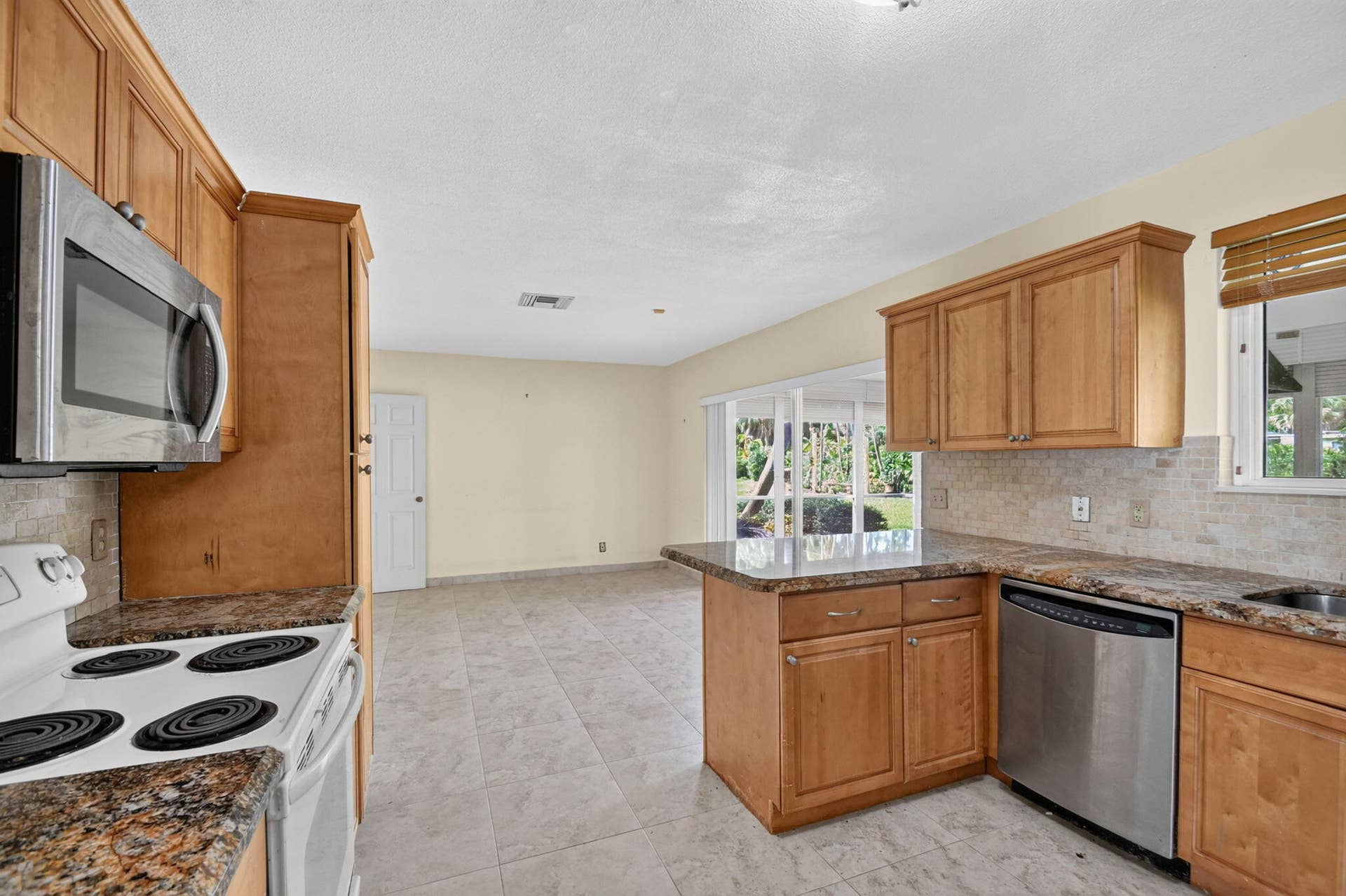 Kitchen with wood cabinetry, granite countertops, tile flooring, and stainless steel appliances