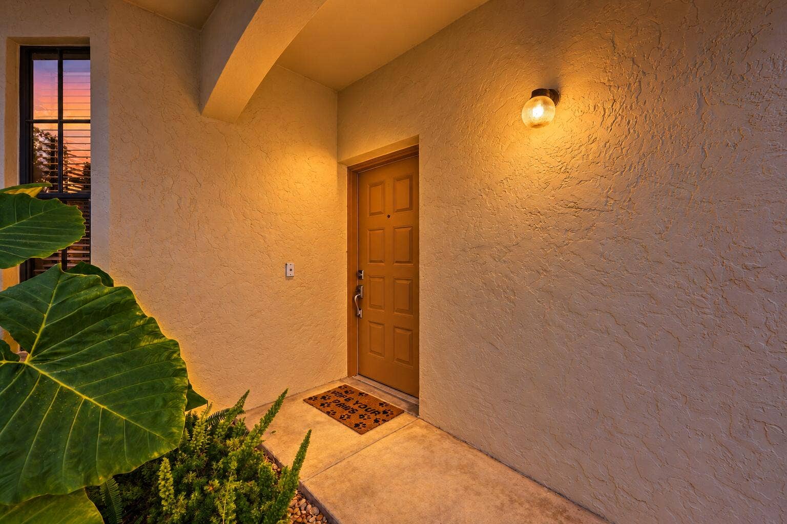 8292 WATERLINE Drive, #106, Boynton Beach, FL 33472 Textured stucco exterior with a paneled entry door, an exterior wall sconce, and a window with horizontal blinds