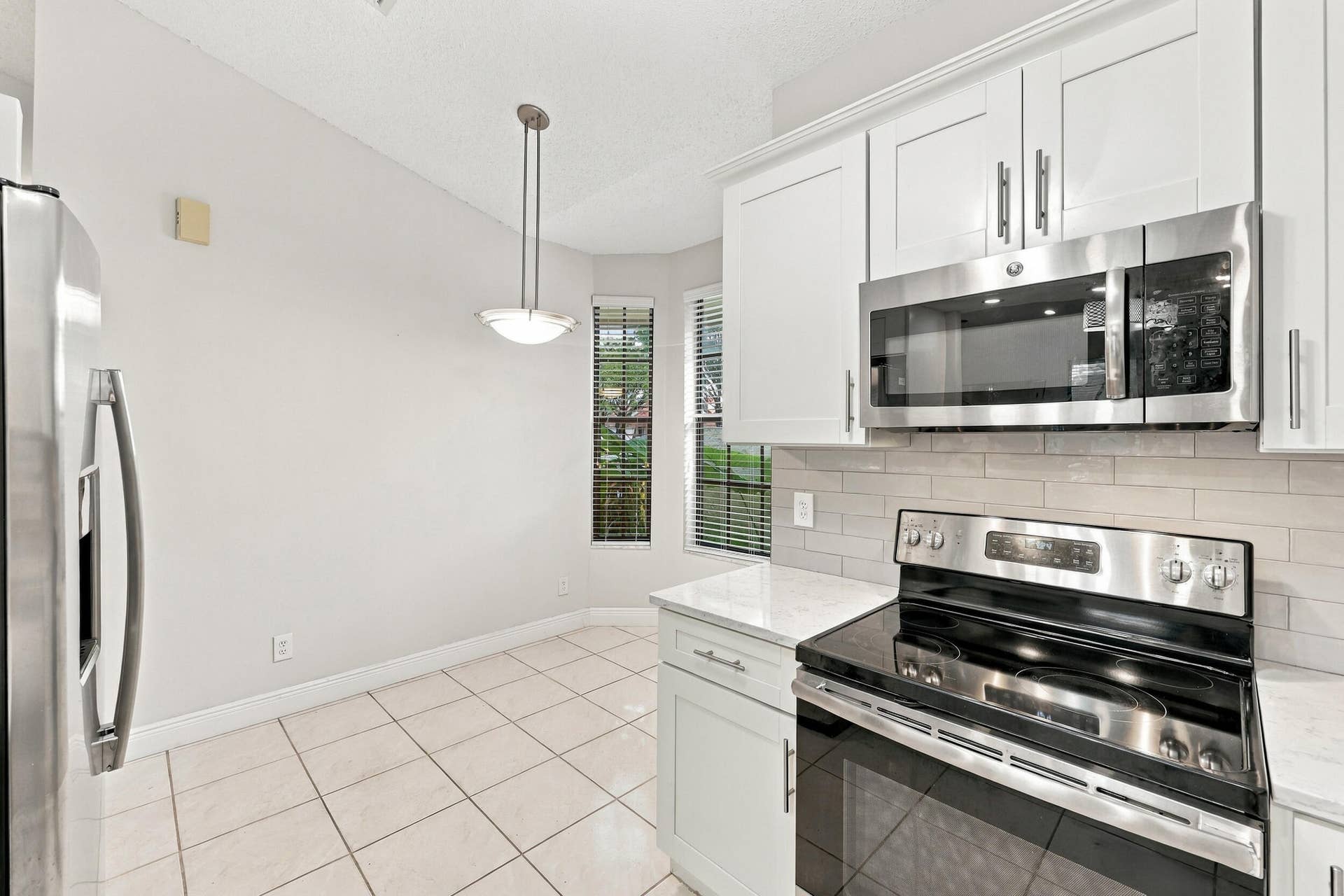 8292 WATERLINE Drive, #106, Boynton Beach, FL 33472 Kitchen featuring white shaker-style cabinetry, stainless steel appliances, a tile backsplash, and light-toned tile flooring