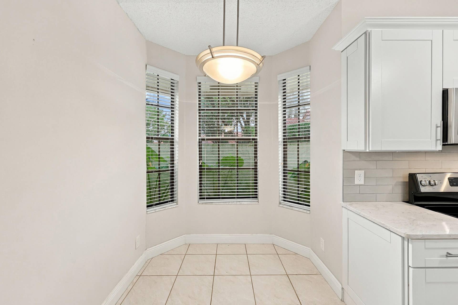 8292 WATERLINE Drive, #106, Boynton Beach, FL 33472 Bay window area with tile flooring, featuring a contemporary pendant light fixture, white cabinetry, and a light-toned countertop