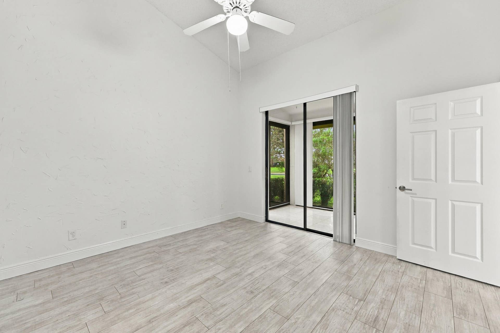 8292 WATERLINE Drive, #106, Boynton Beach, FL 33472 Vaulted ceiling with a white ceiling fan, sliding glass doors to an outdoor area, six-panel interior door, and light wood-finish flooring