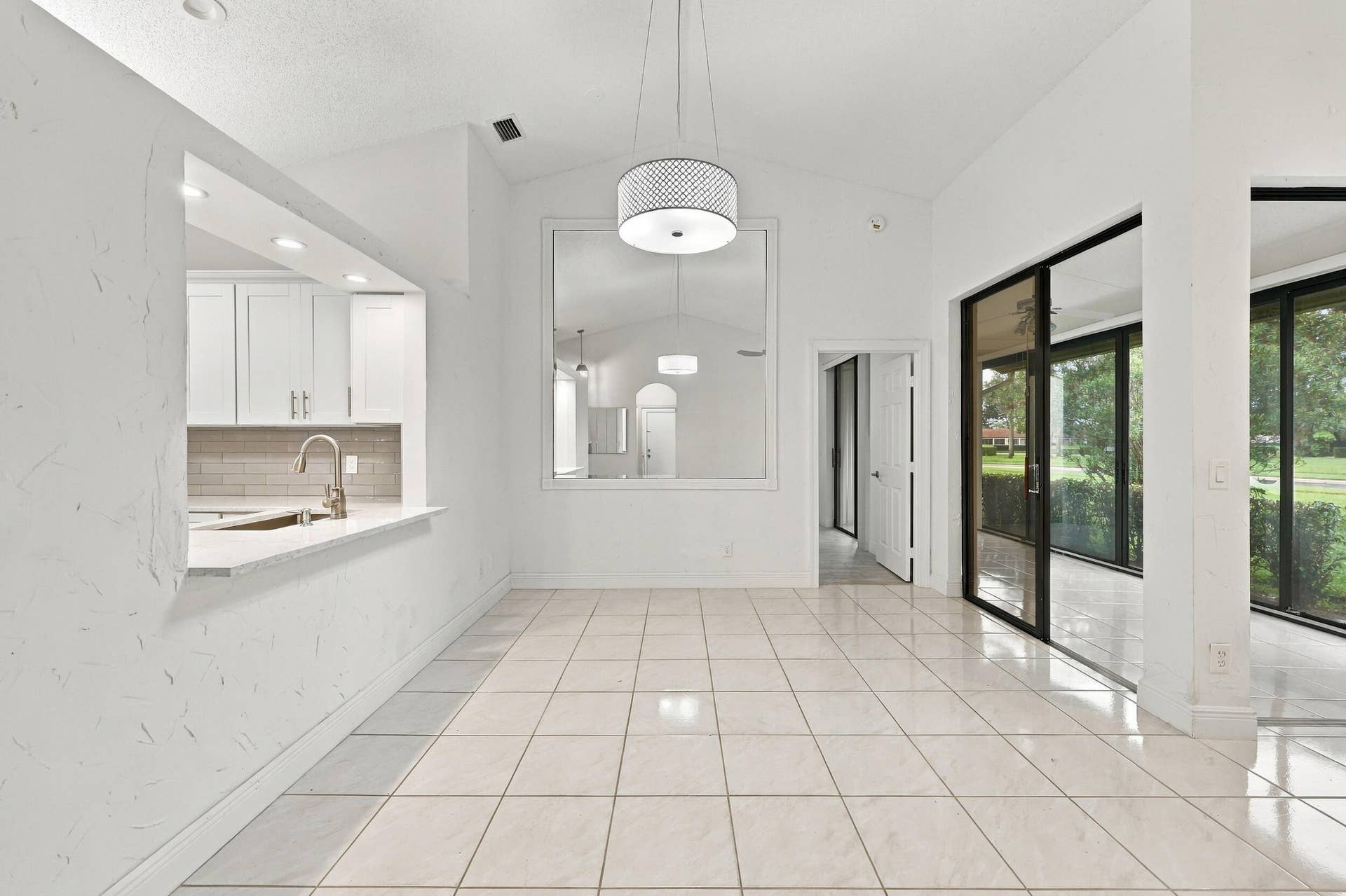 8292 Waterline Drive, #106, Boynton Beach, FL 33472 Vaulted ceilings, tile flooring, modern drum pendant light, white shaker cabinetry, and a kitchen pass-through