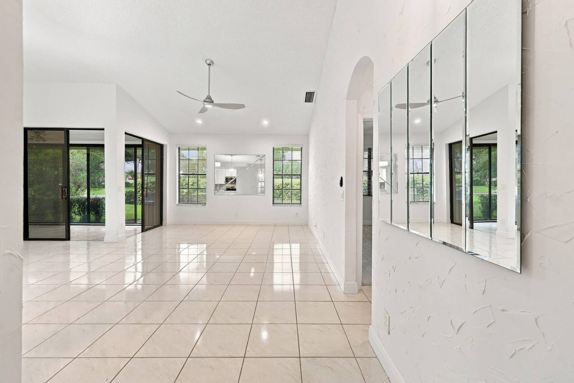8292 Waterline Drive, #106, Boynton Beach, FL 33472 Expansive tiled flooring throughout, modern ceiling fan, large windows with exterior views, built-in wall mirror, and sliding glass doors