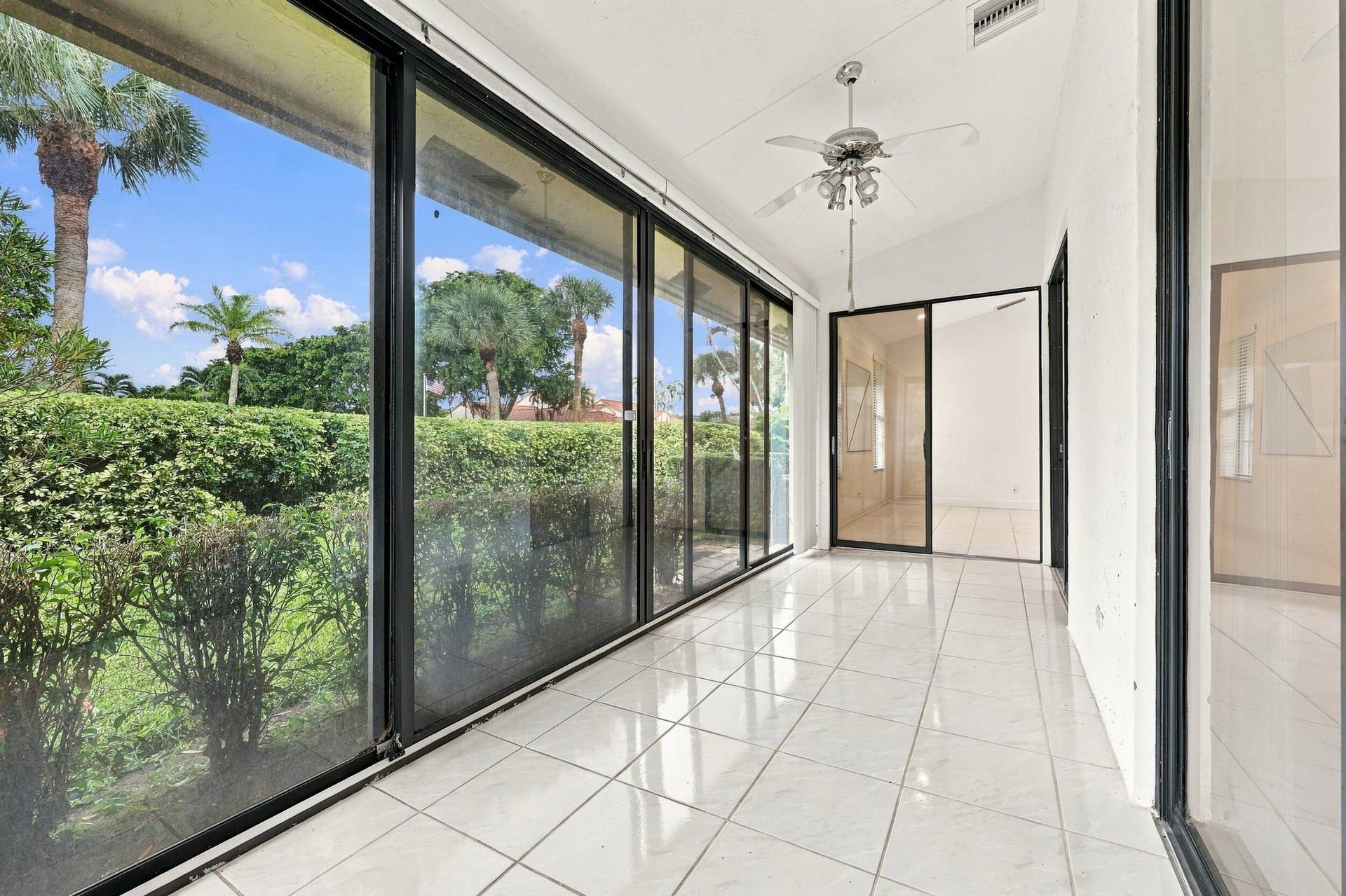8292 Waterline Drive, #106, Boynton Beach, FL 33472 Expansive room with wall-to-wall sliding glass doors, white tiled flooring, a vaulted ceiling, and a ceiling fan with integrated lighting