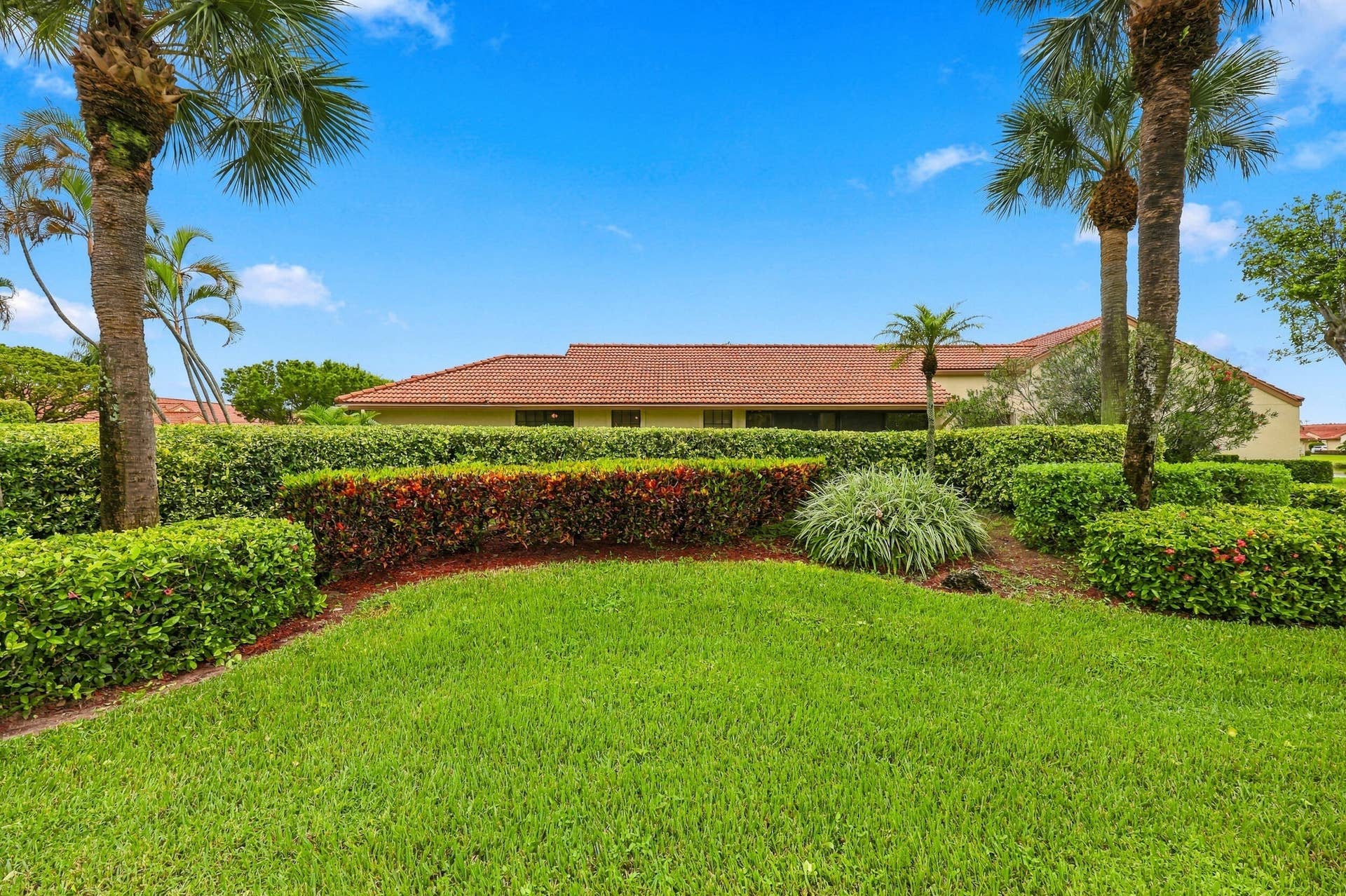 8292 Waterline Drive, #106, Boynton Beach, FL 33472 Expansive green lawn with layered hedges, mature palm trees, and a terracotta tile roof