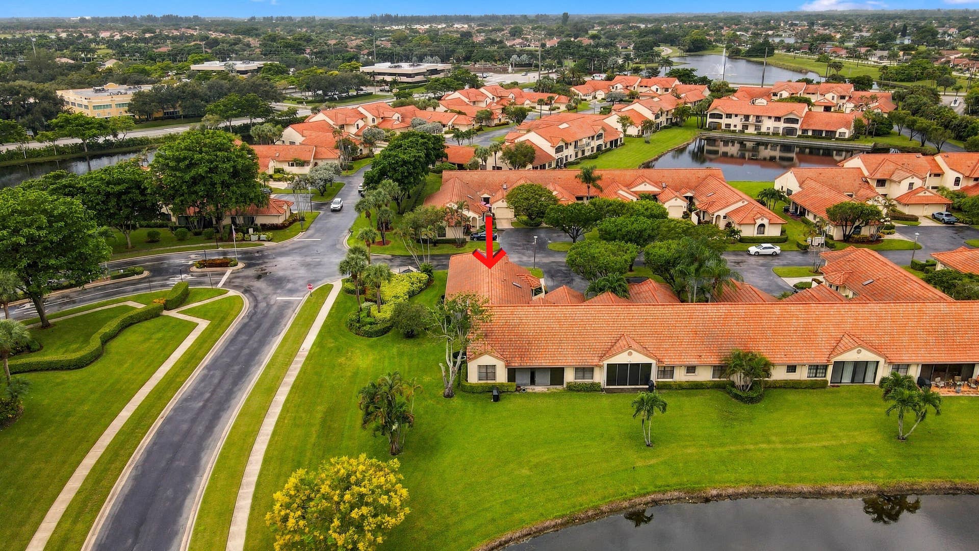 8292 Waterline Drive, #106, Boynton Beach, FL 33472 Terracotta tile roof structure with a manicured green lawn, surrounded by mature trees, and a pond