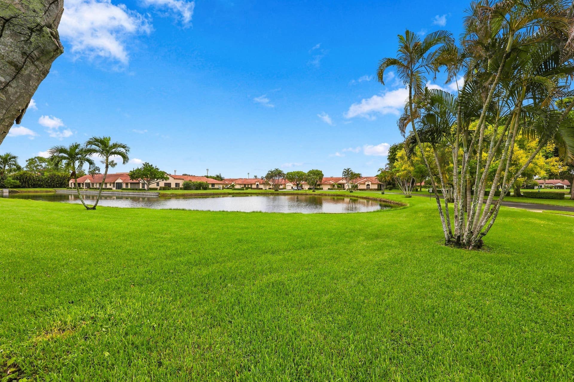 8292 Waterline Drive, #106, Boynton Beach, FL 33472 Expansive green space featuring a tranquil water body, mature palm trees, and residential structures with terracotta-style roofs
