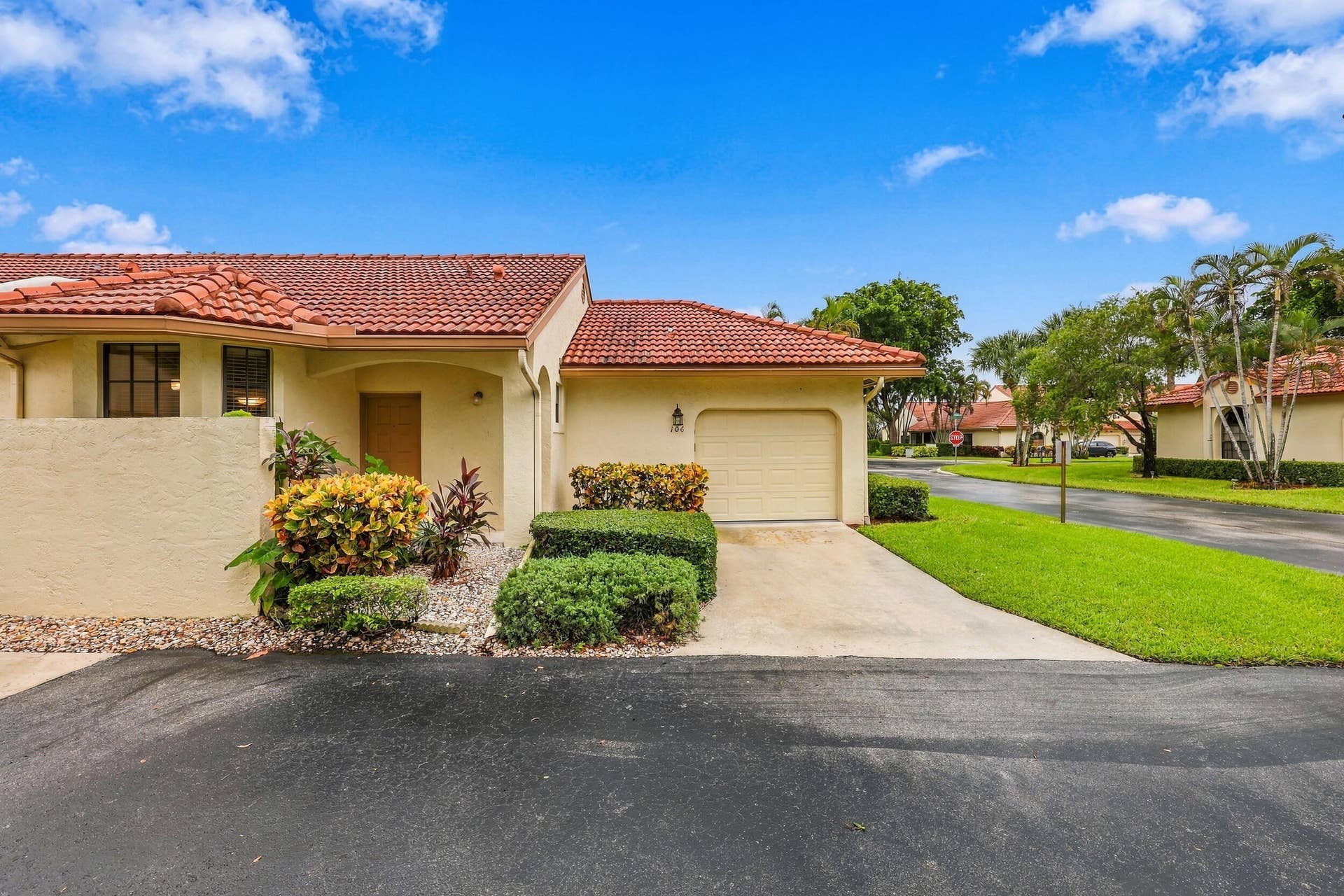 8292 Waterline Drive, #106, Boynton Beach, FL 33472 Mediterranean-style exterior with a terracotta tile roof, stucco finish, attached garage, concrete driveway, and established landscaping