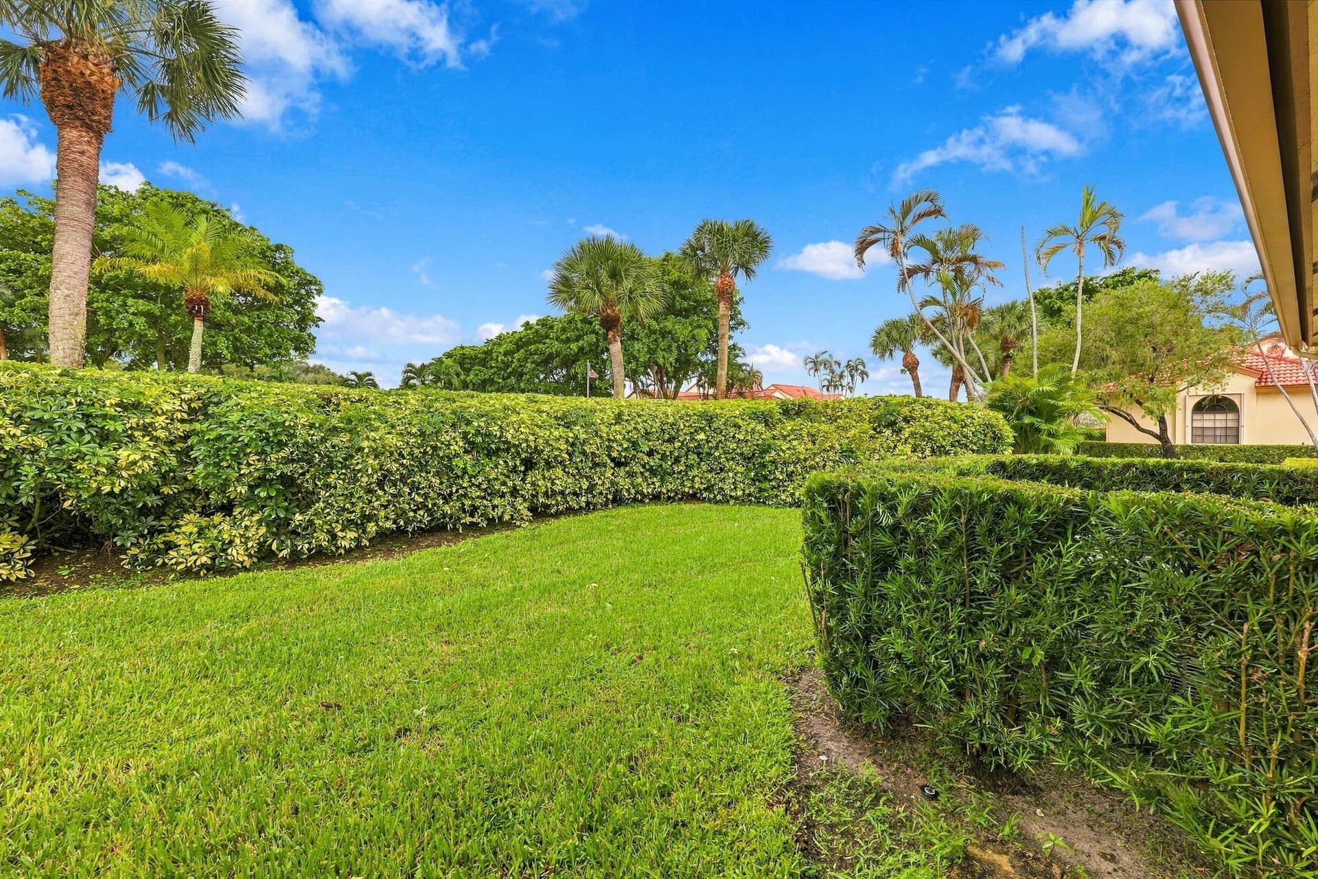 8292 Waterline Drive, #106, Boynton Beach, FL 33472 Manicured landscaping with hedge privacy, green lawn, and tropical palm trees