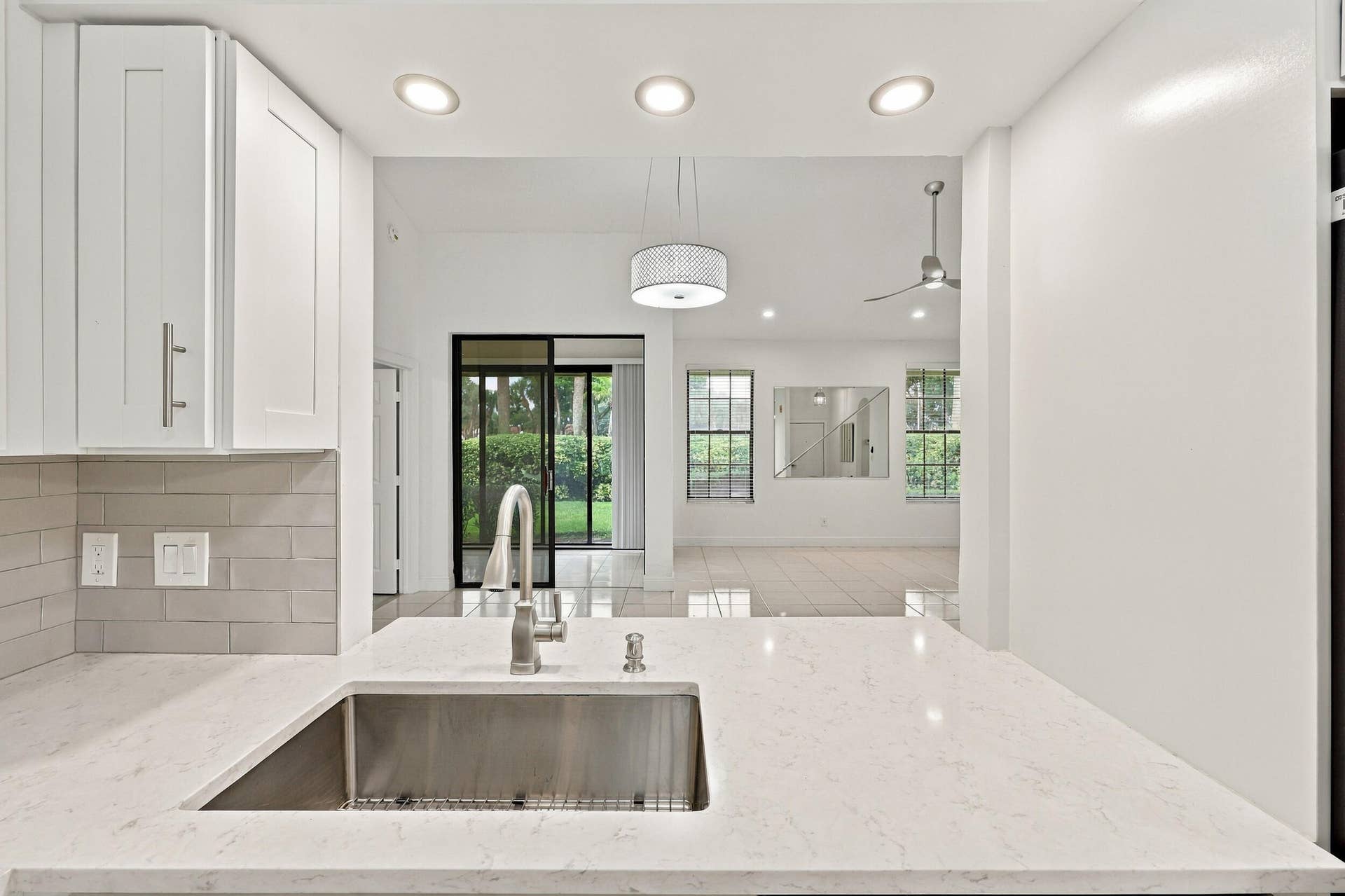 8292 Waterline Drive, #106, Boynton Beach, FL 33472 Kitchen featuring a stainless steel sink, light-toned countertop, white cabinetry, and subway tile backsplash