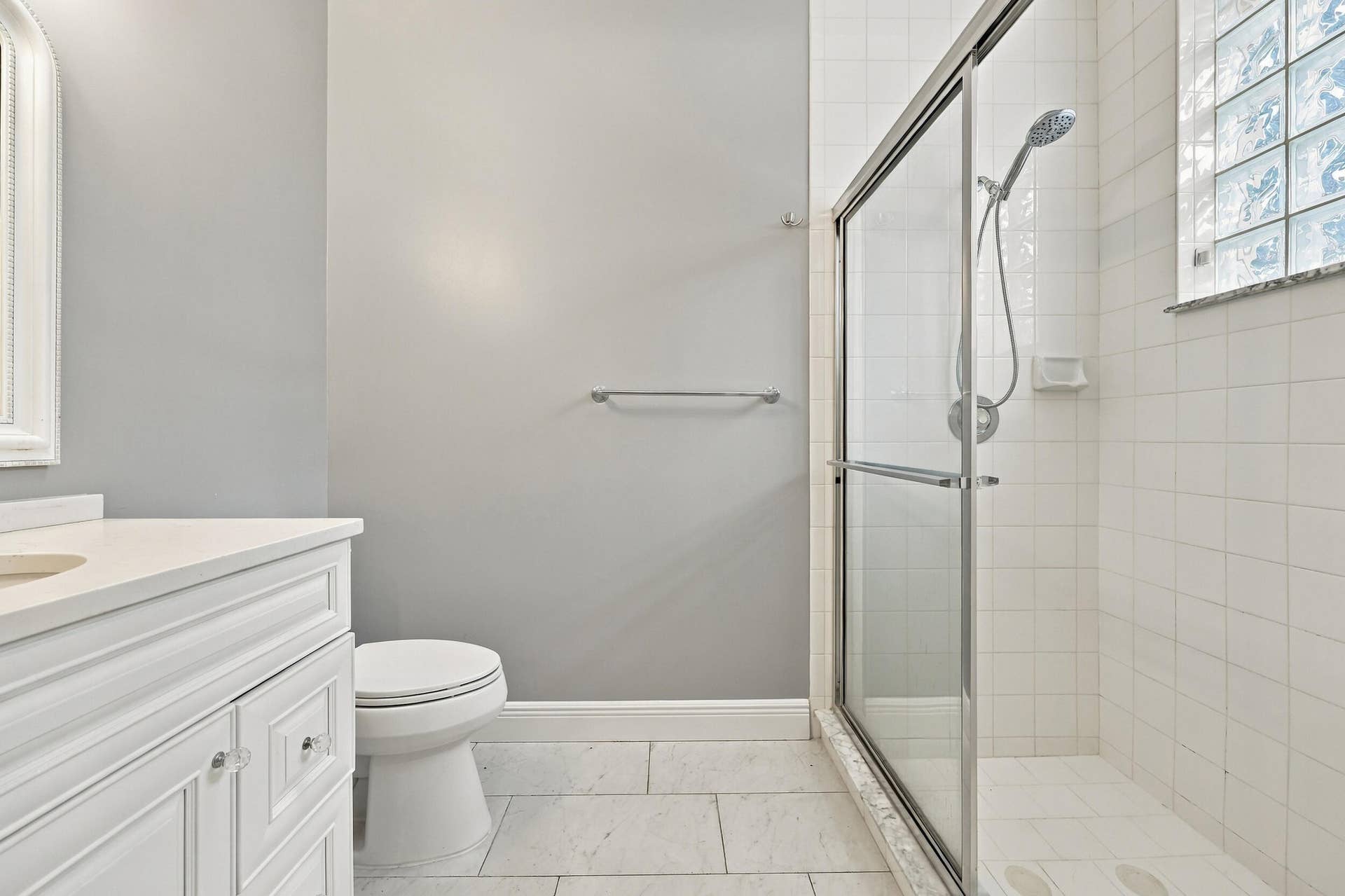8292 Waterline Drive, #106, Boynton Beach, FL 33472 White vanity with clear knob hardware, white countertop, tile flooring, glass-enclosed shower, and block window