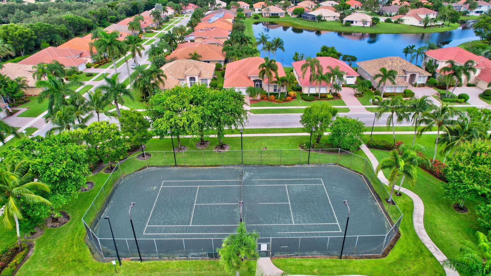 6610 Aston Lane, Boynton Beach, FL 33437 Tennis court with perimeter fencing, surrounded by manicured lawn and mature trees
