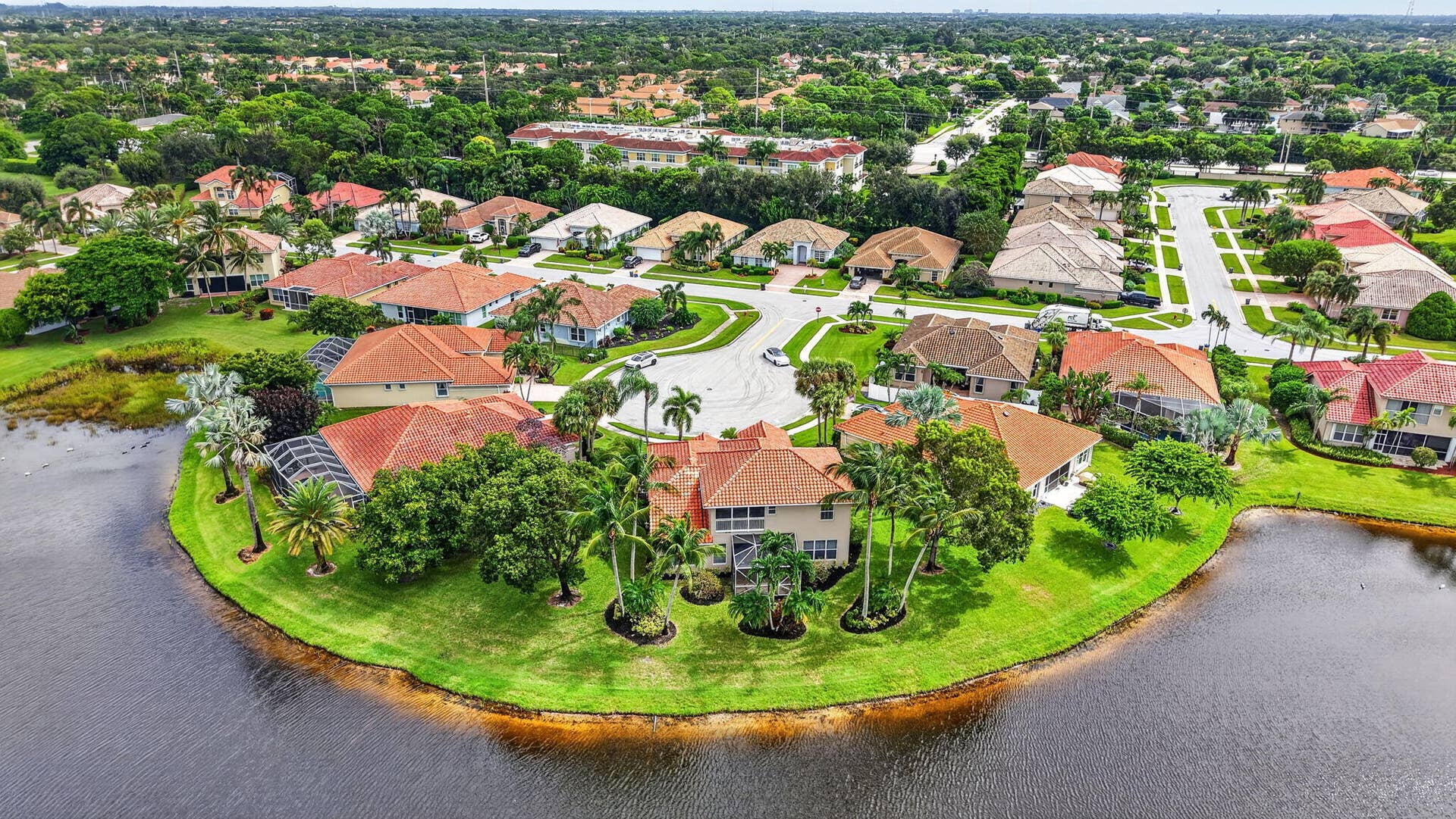 6610 Aston Lane, Boynton Beach, FL 33437 Residential properties featuring tile roofs and screened enclosures, situated on landscaped lots with mature trees, bordering a body of water within a developed community