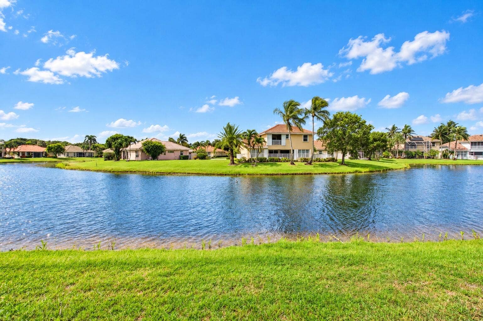 6610 Aston Lane, Boynton Beach, FL 33437 Expansive water frontage with lush green lawn, mature palm trees, and tropical landscaping surrounding the property