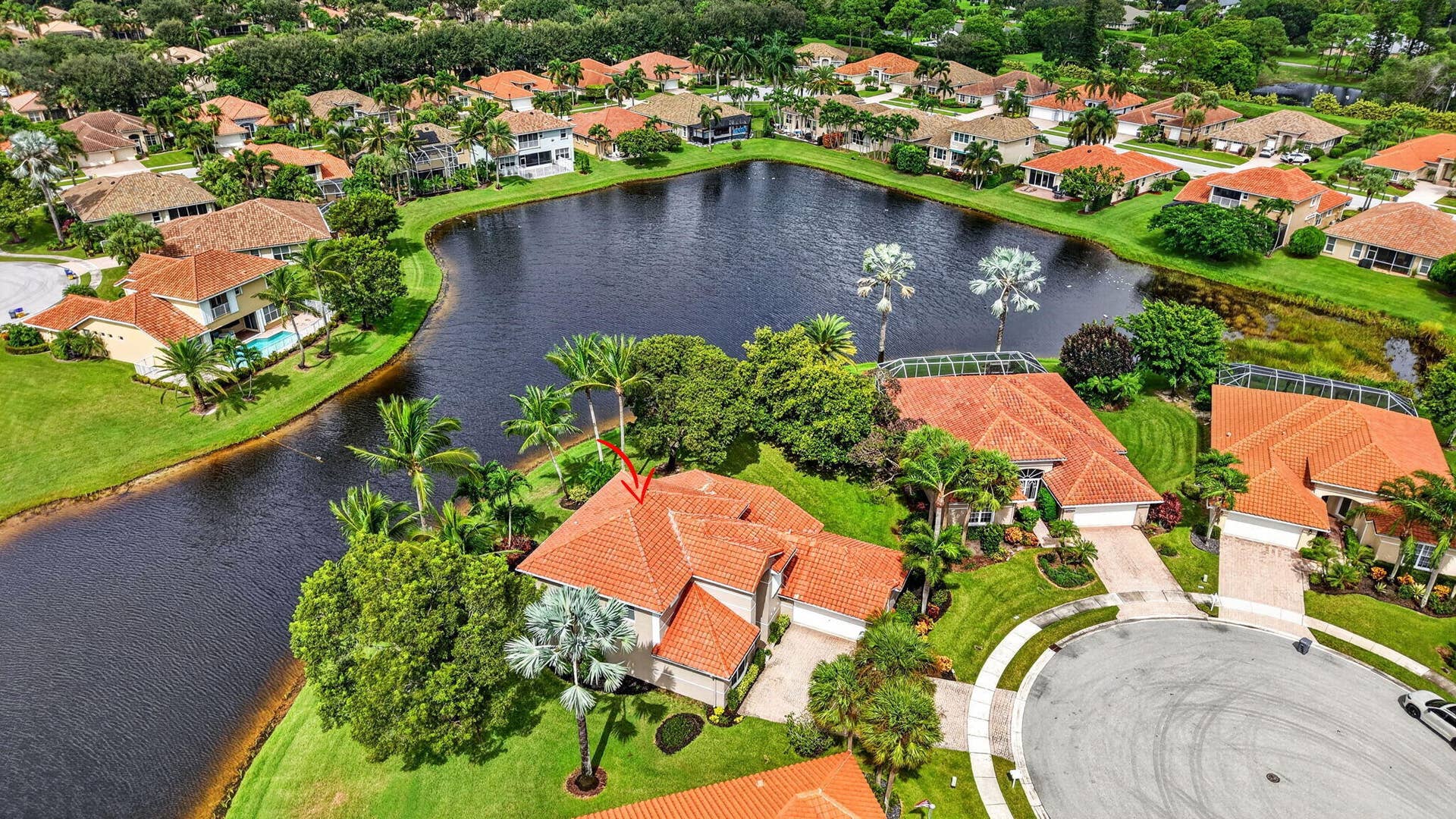 6610 Aston Lane, Boynton Beach, FL 33437 Waterfront property with a red tile roof, lush green landscaping, and mature palm trees