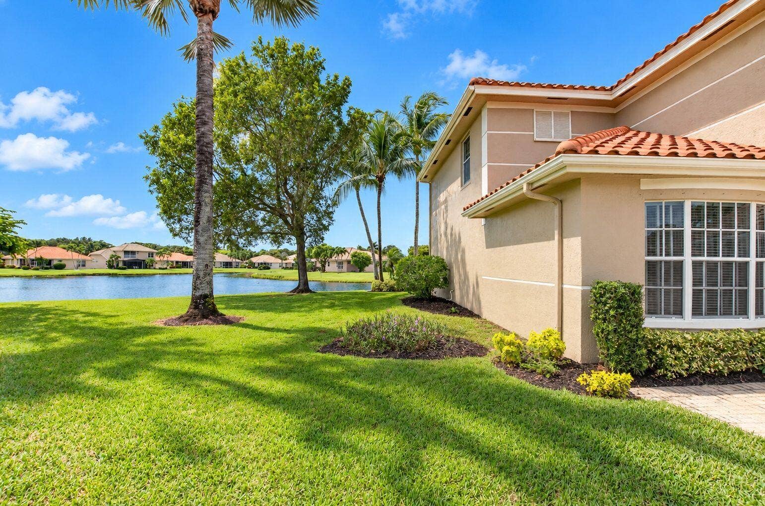 6610 Aston Lane, Boynton Beach, FL 33437 Stucco exterior with a terracotta tile roof, bay window, landscaped planting beds, and a paver walkway