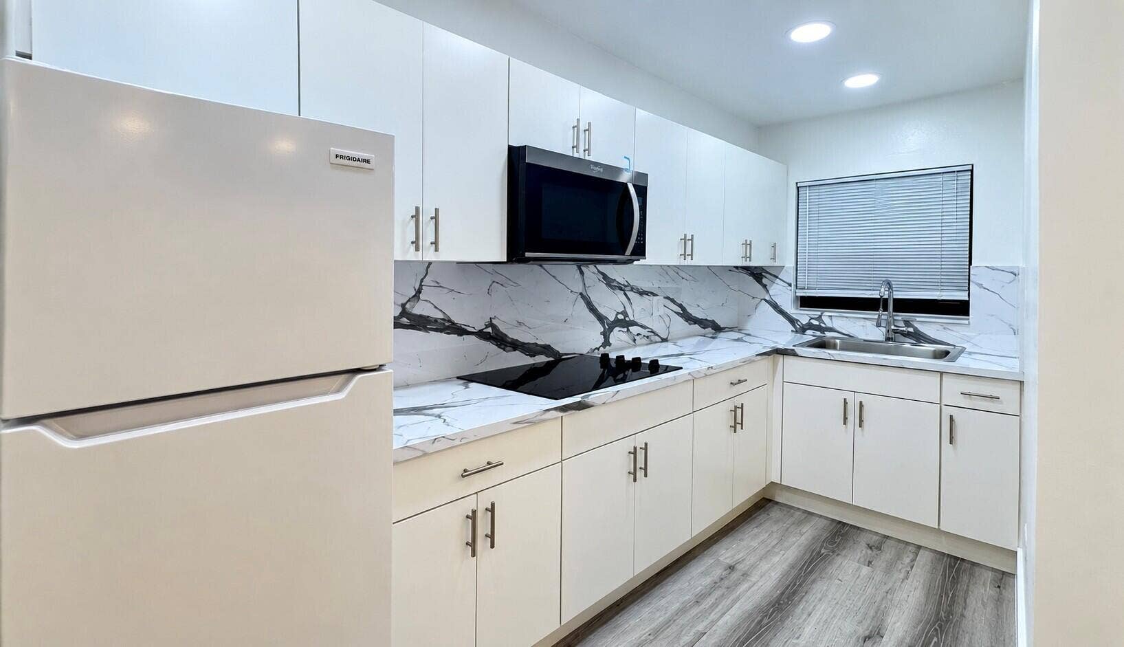 560 NE 15th Avenue, Fort Lauderdale, FL 33301 White cabinetry with contemporary hardware, a built-in microwave, wood-finish flooring, a stainless-steel sink, and a black cooktop. Virtually staged.