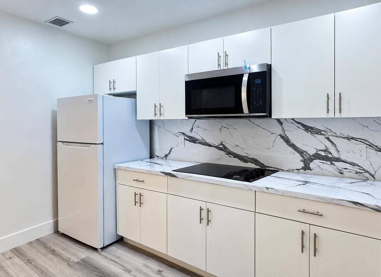 560 NE 15th Avenue, Fort Lauderdale, FL 33301 White cabinetry with brushed nickel hardware, striking veined countertop and backsplash, built-in microwave, and wood-finish flooring. Virtually staged.