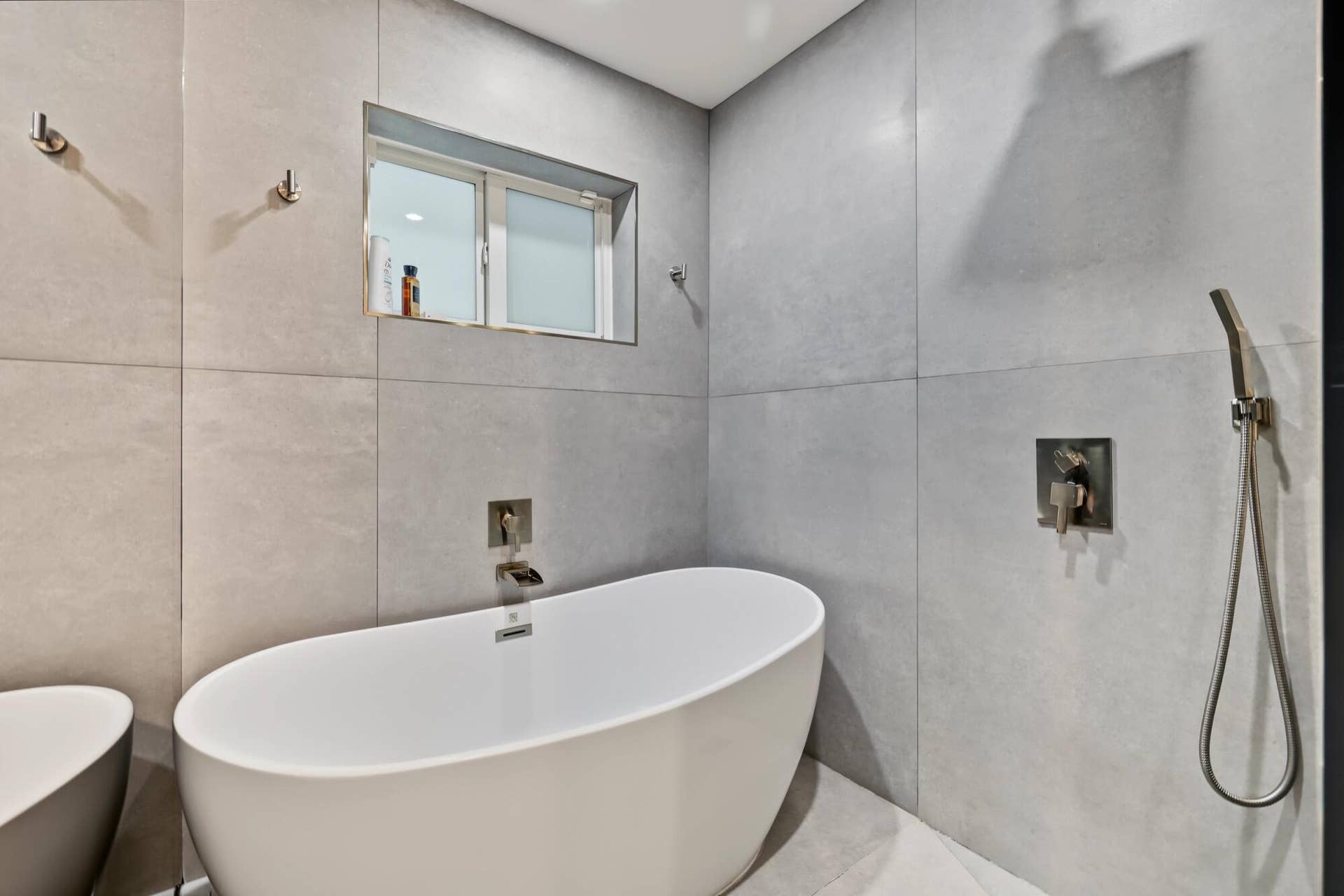 1311 SE 4TH Avenue, Pompano Beach, Pompano Beach, FL 33060 Freestanding soaking tub with brushed nickel fixtures, surrounded by large format wall tiling and a built-in window