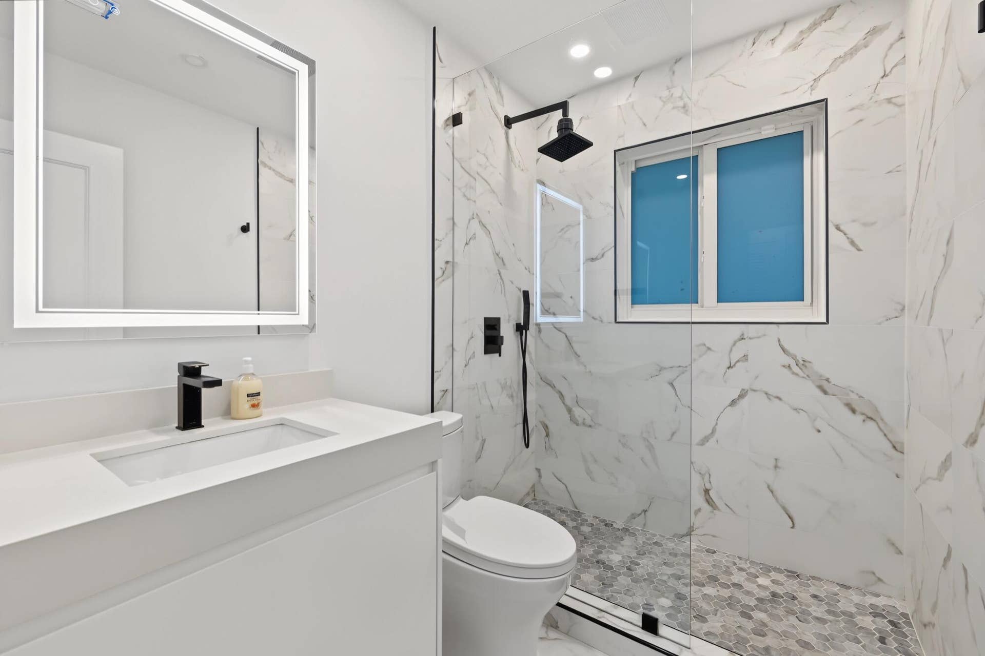 1311 SE 4TH Avenue, Pompano Beach, Pompano Beach, FL 33060 Vanity with integrated sink and matte black faucet, illuminated mirror, walk-in shower with glass enclosure, rain shower fixture, and hexagonal floor tiling, and a window for natural light