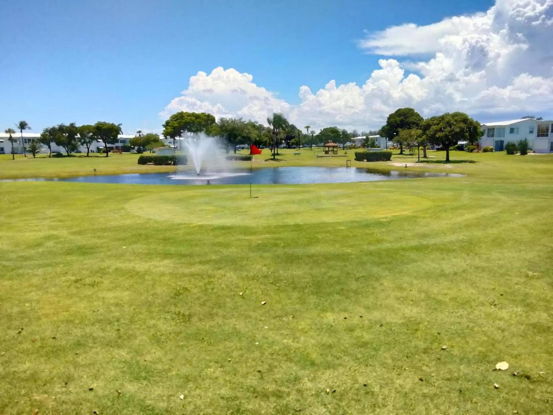 Expansive green golf course with a central water feature, fountain, and surrounding residences