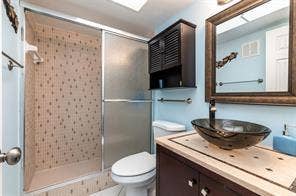 Shower enclosure with sliding glass doors, built-in vanity with vessel sink, framed mirror, and mounted storage cabinet